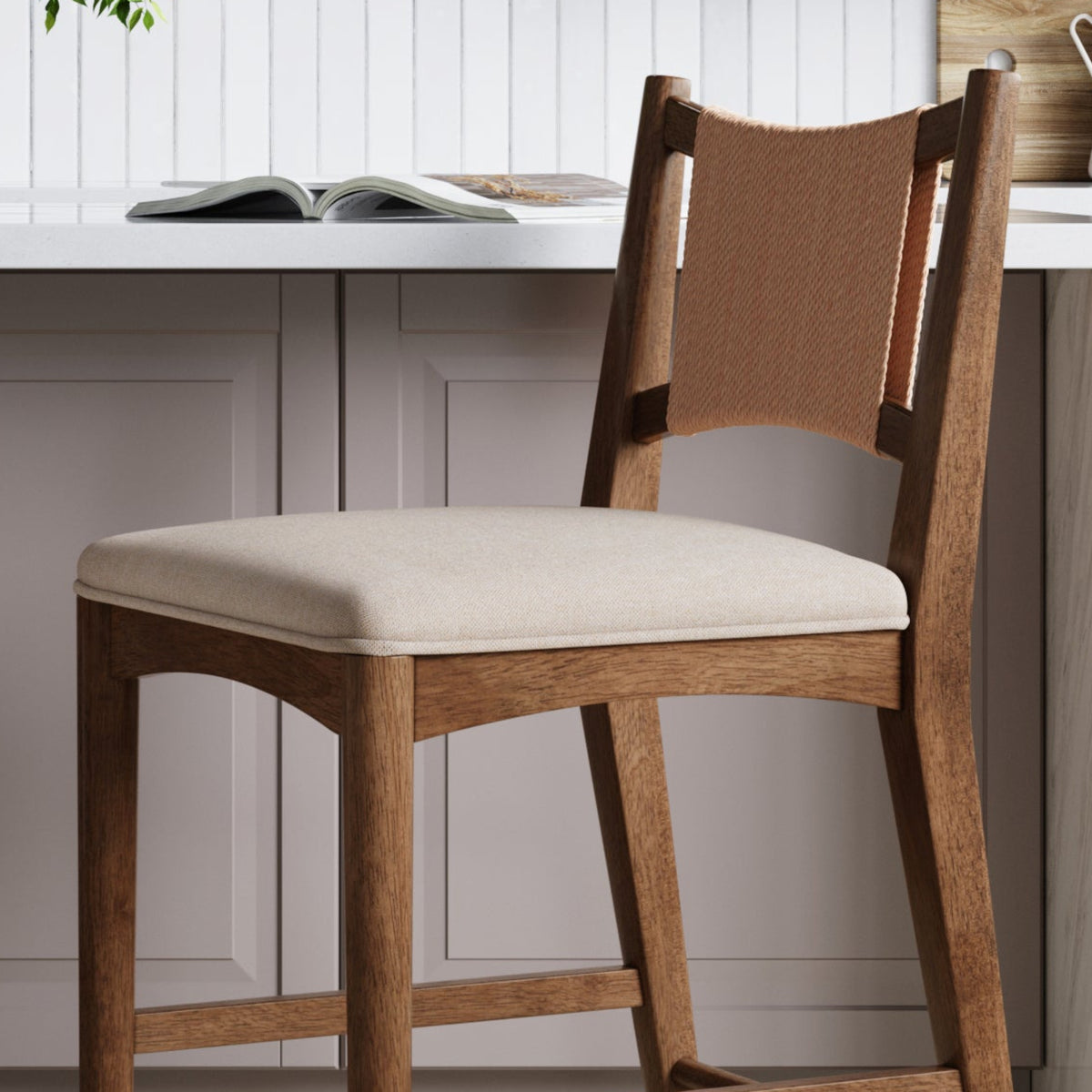 Wooden counter stool with a padded cream seat and a woven backrest, positioned in a kitchen.