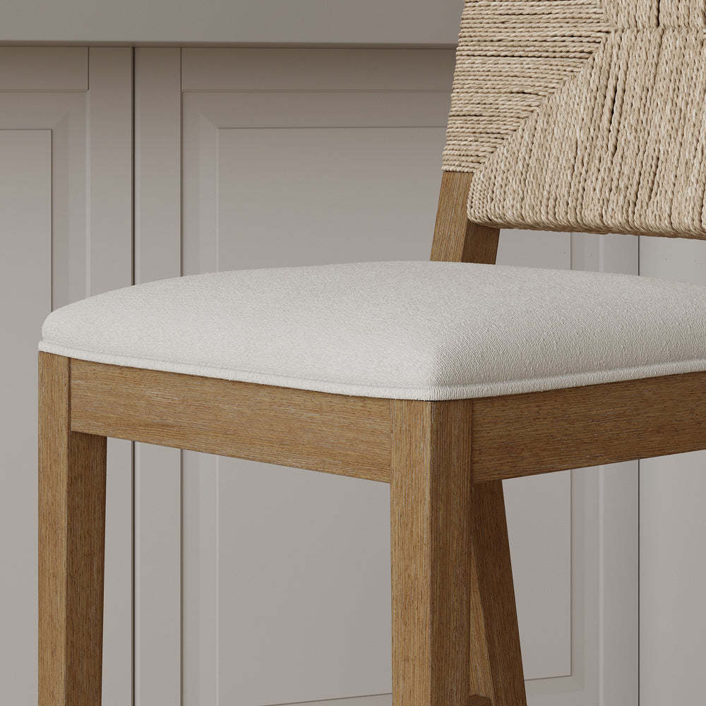 A wooden stool with a light-colored upholstered seat and a woven rope backrest.