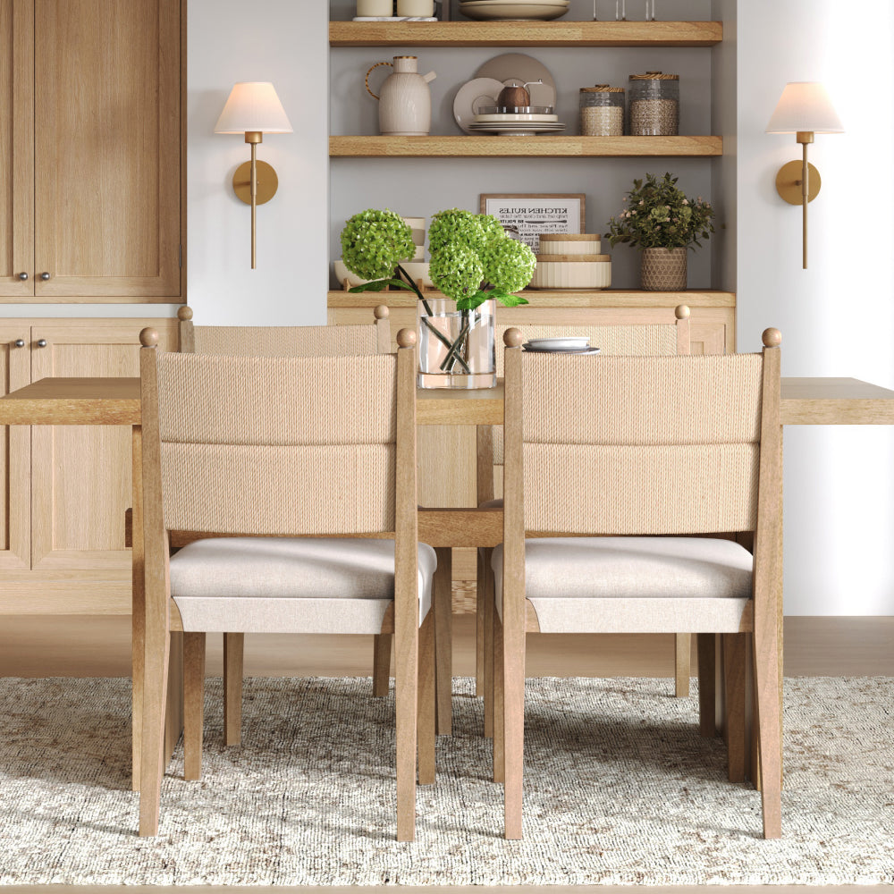A light wood dining table with four chairs featuring rope-wrapped backrests and fabric-covered seats, set in front of open shelves and cabinetry.