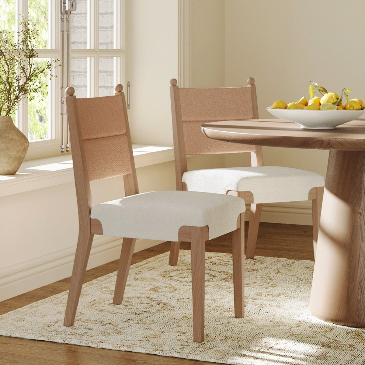 Two wooden dining chairs with light-colored upholstered seats and woven backrests positioned near a round wooden table.