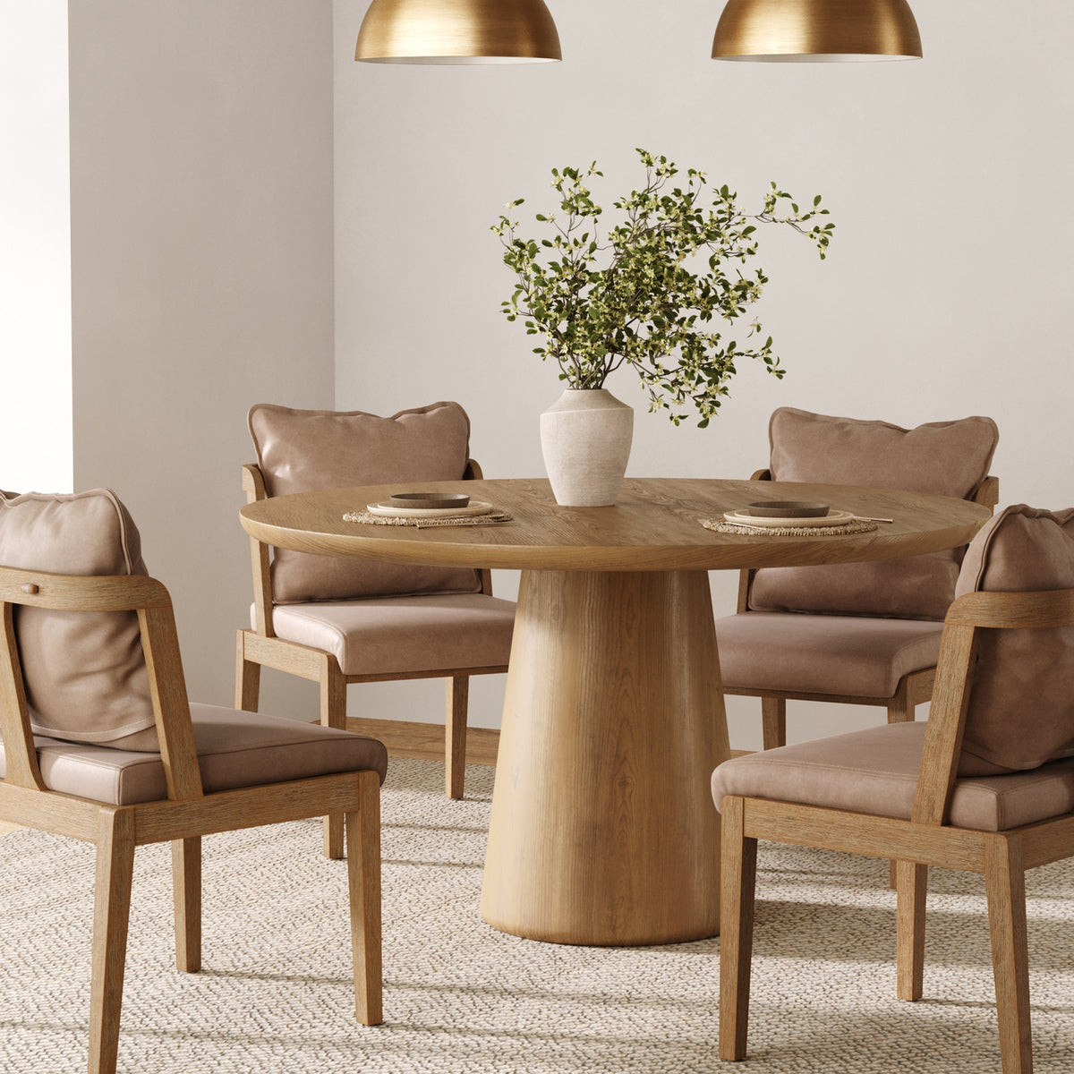 A round wooden dining table with a vase of greenery and four upholstered chairs on a textured rug.
