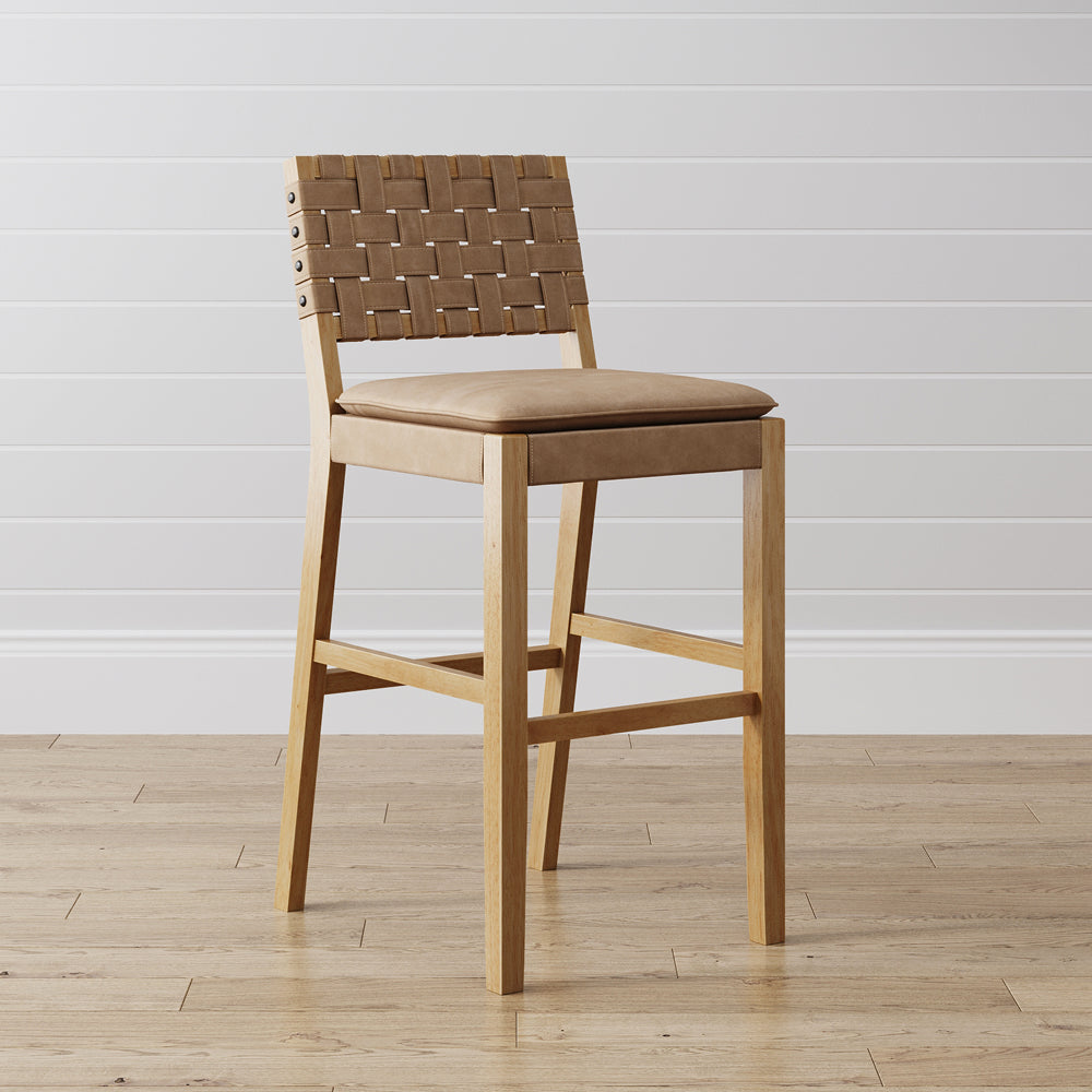 Light wood bar stool with a woven tan leather backrest and a cushioned seat.