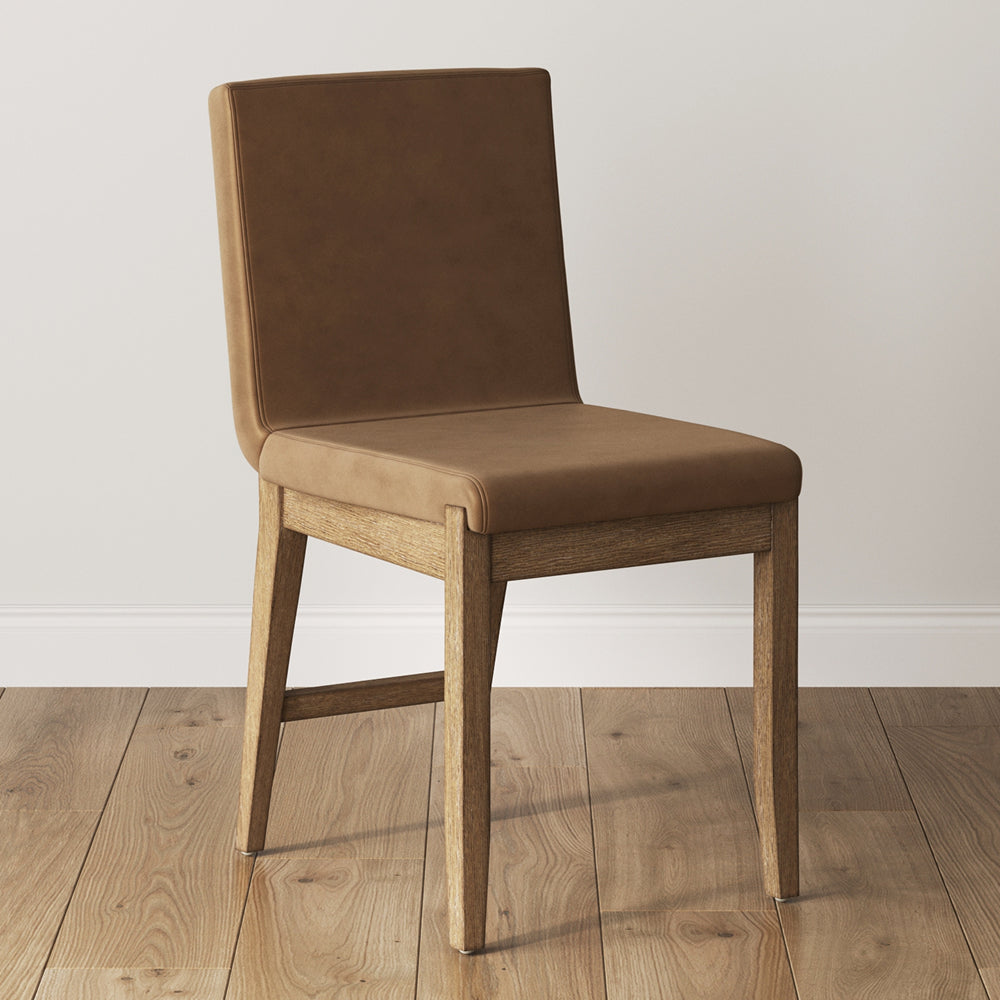 Armless dining chair with a brown upholstered seat and back on a light wood frame.