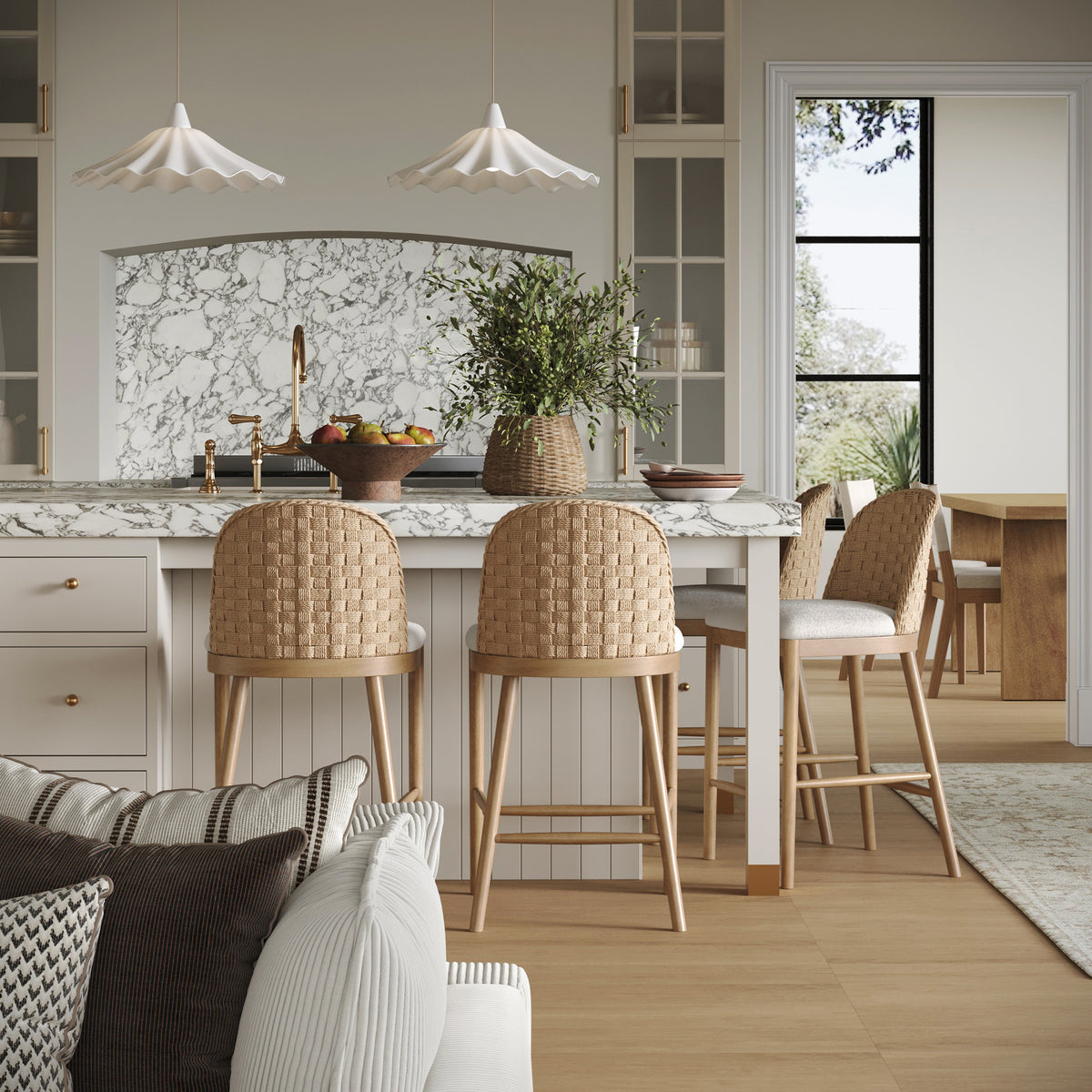 A kitchen island with a marble countertop, three woven bar stools, and a fruit bowl, viewed from a living area.