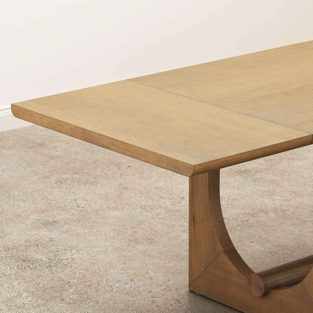Close-up of a Nathan James Mid-Century Modern Table Leaf Extensions Light Brown, featuring a light brown finish, a visible extension leaf seam, and a curved pedestal base.
