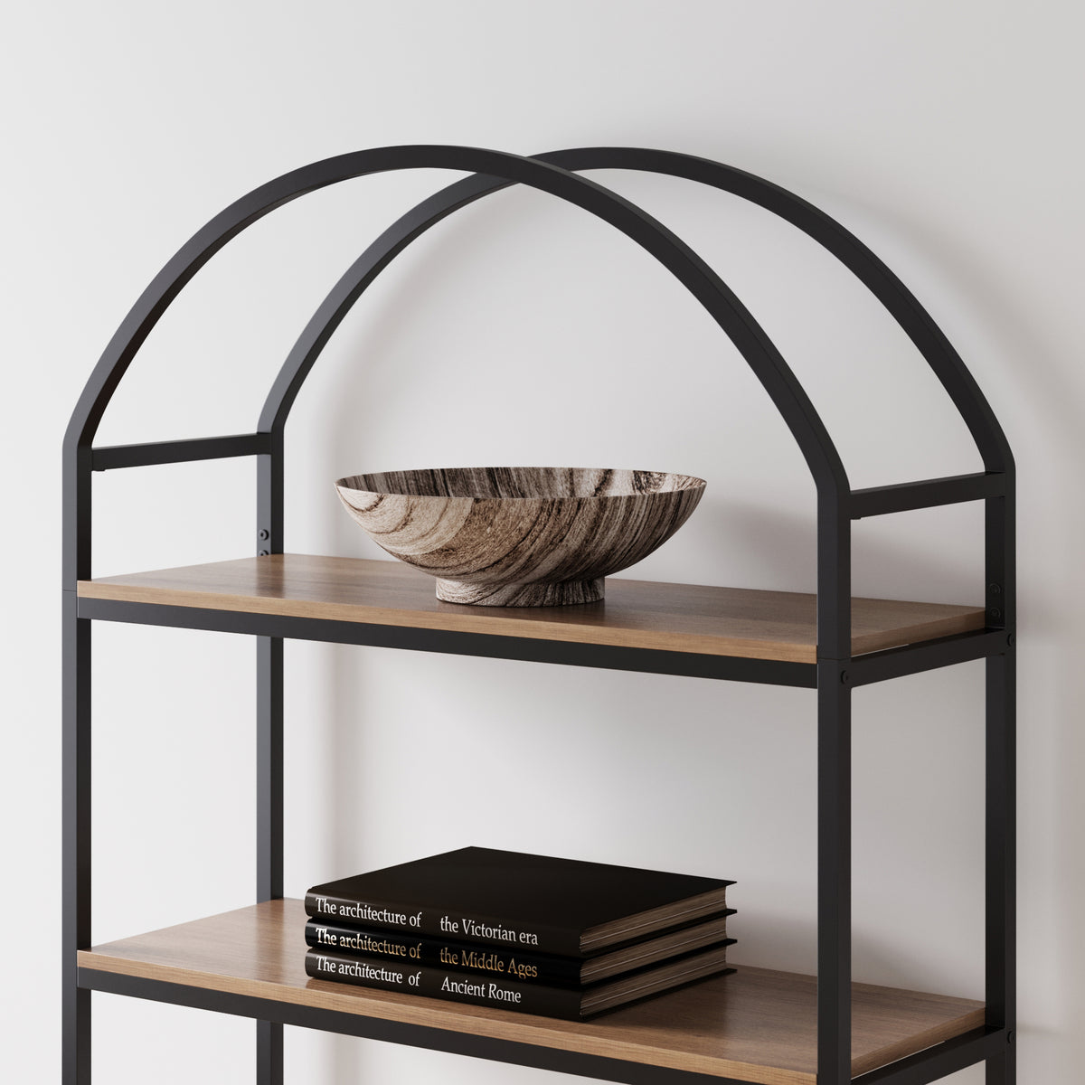 A black metal arched bookshelf with wood-toned shelves, featuring a decorative bowl on the top shelf and a stack of three history books on the lower shelf.