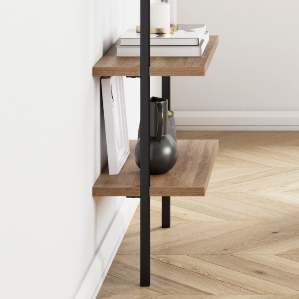 A tall shelving unit with two wooden shelves supported by a black metal frame, holding books, a candle, and decorative objects.