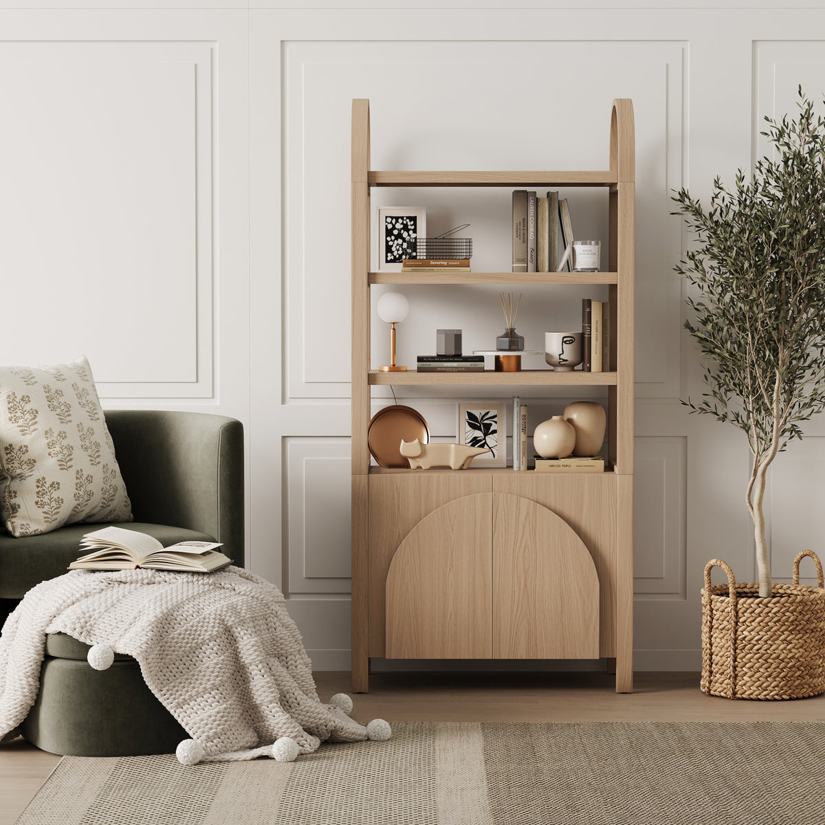 A wooden bookshelf with open shelves holding decorative objects and books stands next to a green armchair with an open book and a knit blanket.