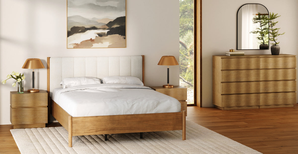 A wooden bed frame with a white tufted headboard, flanked by two matching nightstands with gold lamps, in a bedroom with a dresser and an arched mirror.