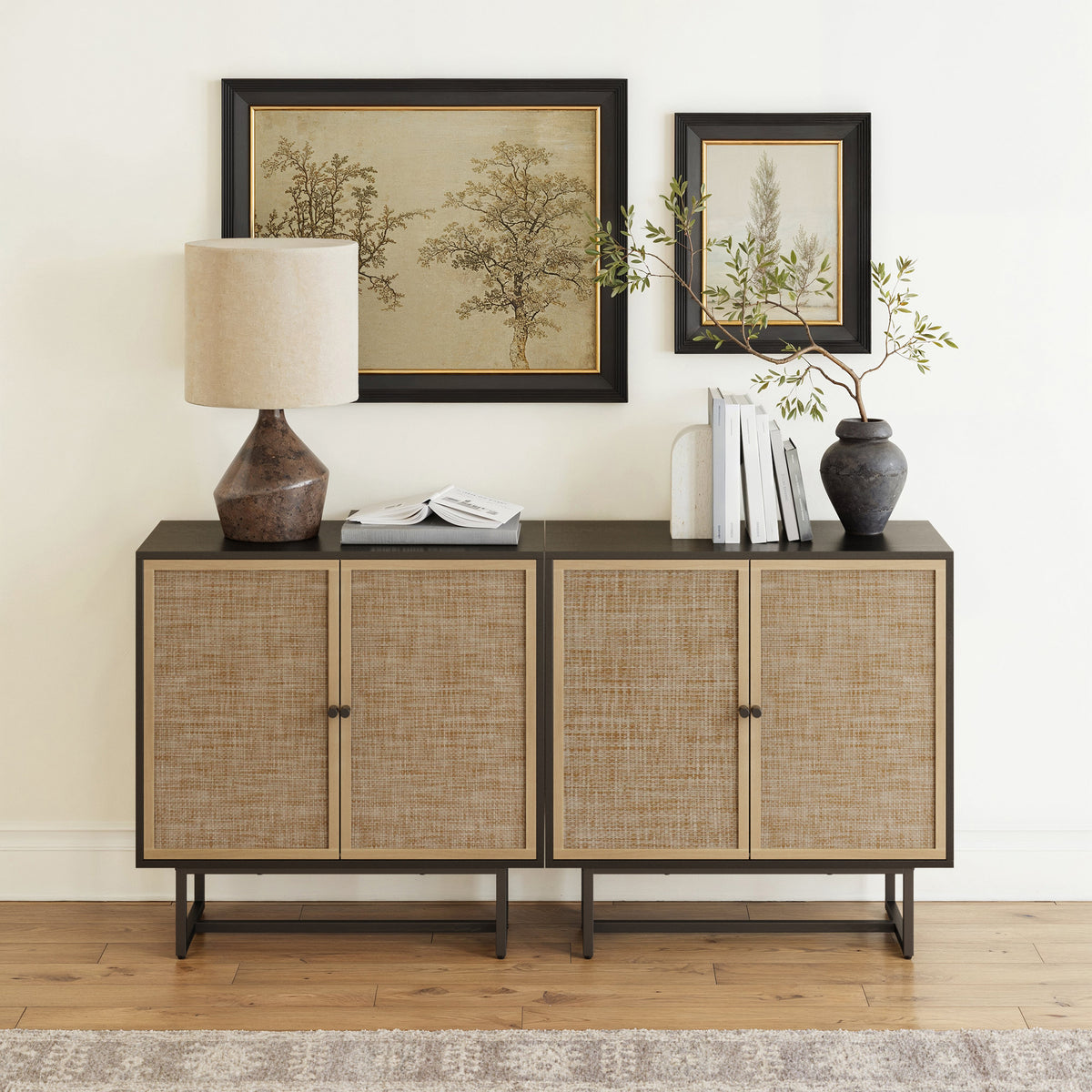 Two side-by-side black Nathan James Rattan Storage Cabinet Credenza units with woven textilene doors, topped with a table lamp, books, and a vase.