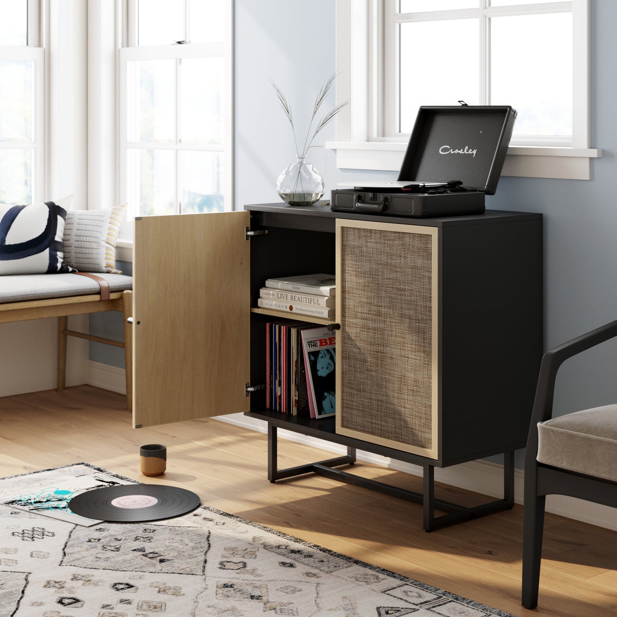 A black record player sits on a black cabinet with a partially open door, revealing books and vinyl records inside.