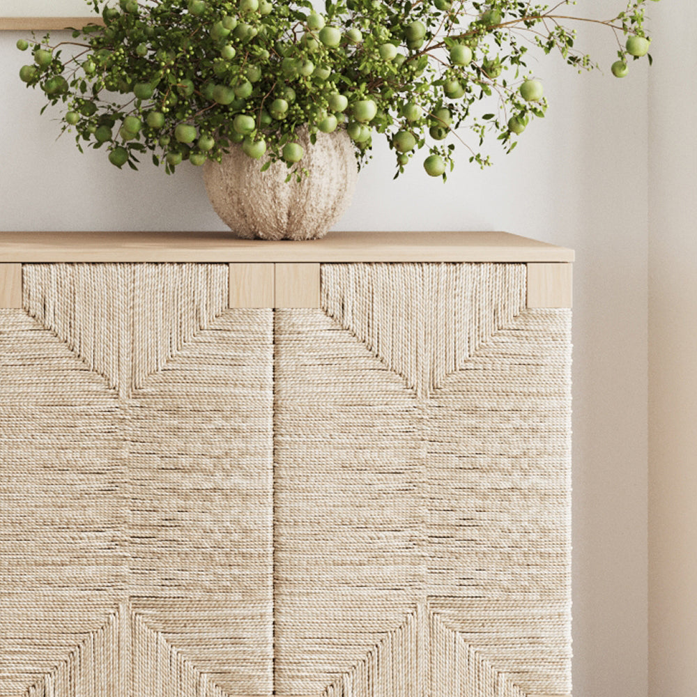 A cabinet with doors wrapped in patterned light-colored rope, topped with a vase of green fruit-bearing branches.
