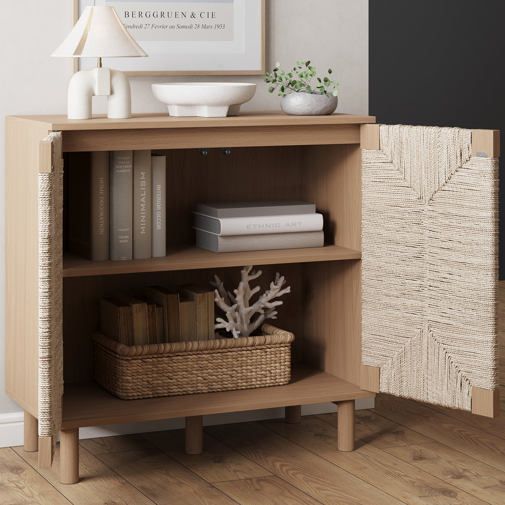 A light wood storage cabinet with open doors and two interior shelves holding books, a woven basket, and a decorative coral piece.