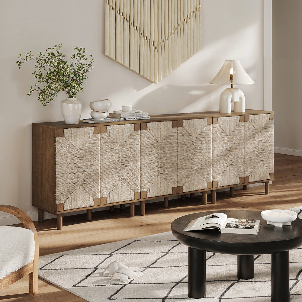 Long wooden sideboard with four woven panel doors, topped with a vase of greenery, a lamp, and a stack of books.