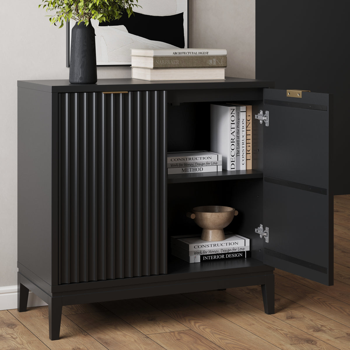 Black sideboard with a fluted cabinet door and an open section displaying stacked books and a small bowl.