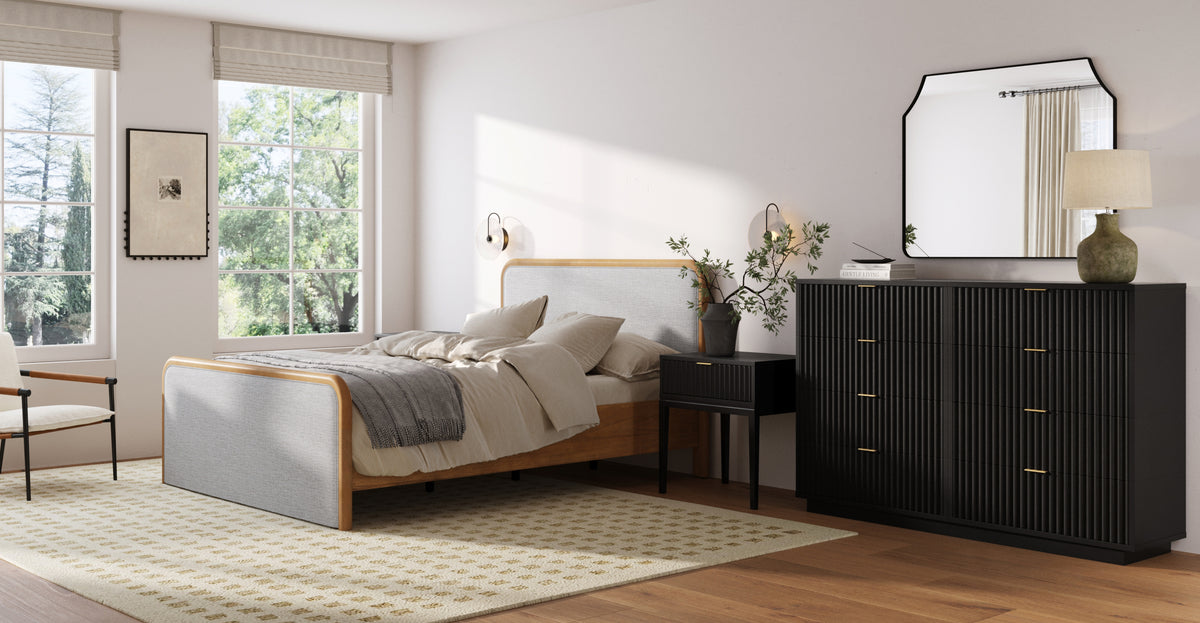 A bedroom featuring a light wood and grey fabric bed, a black ribbed dresser with a mirror, and a matching black nightstand.