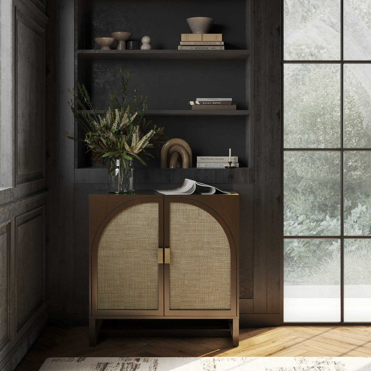 A dark wood cabinet with two arched cane-front doors stands beneath built-in shelving filled with books and decorative objects.