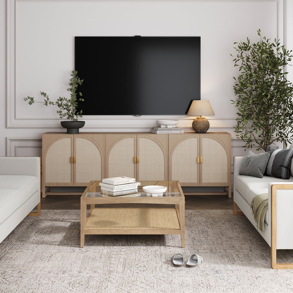 A living room featuring a wall-mounted television above a long light-wood media console with arched cane doors, a matching coffee table with a glass top, and two sofas facing each other.
