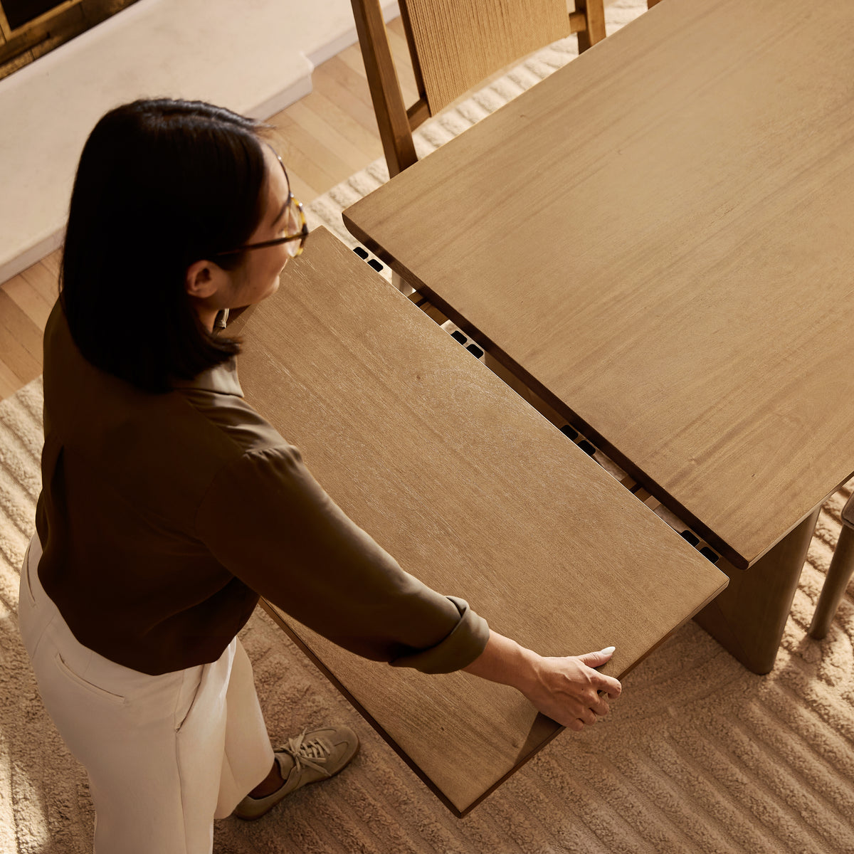 A woman extending a wooden dining table by sliding a leaf into place.