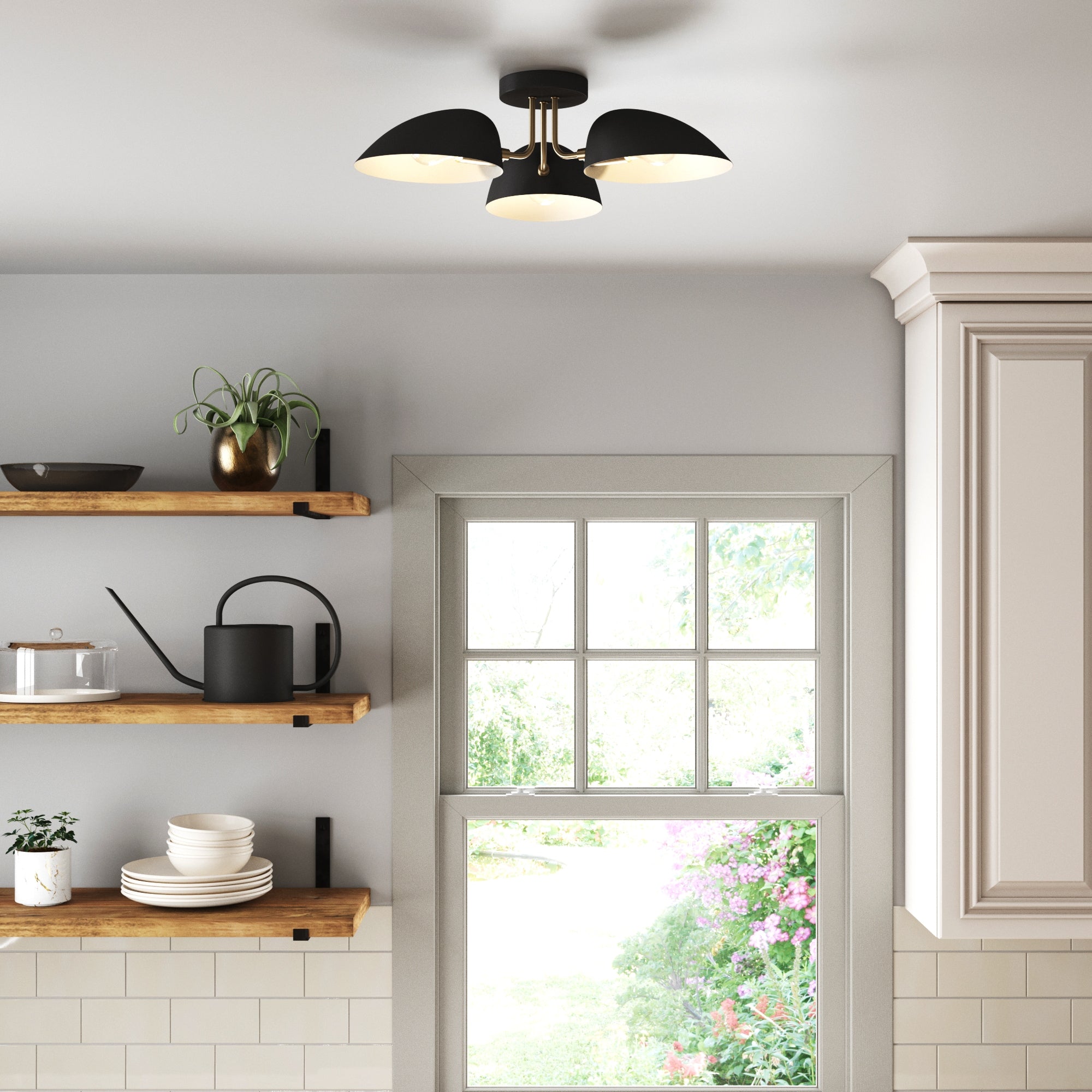 A modern kitchen with floating wooden shelves holding dishes, a watering can, and a potted plant. A window overlooks a garden, and a black ceiling light with three dome-shaped shades is mounted above.