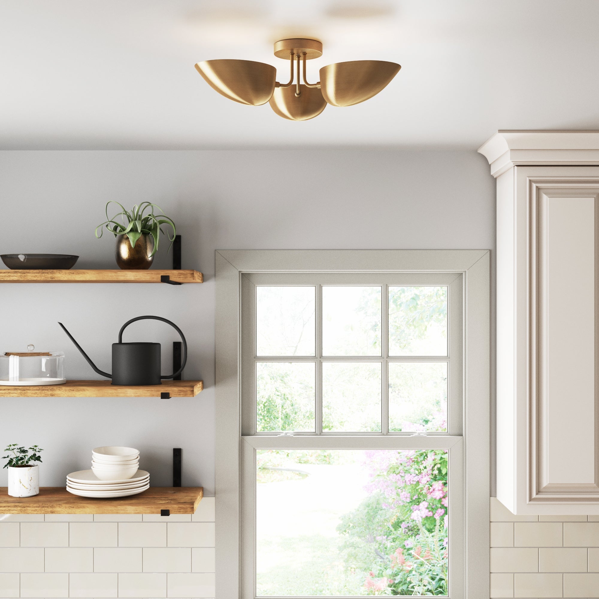 A modern kitchen with light gray walls, wooden floating shelves holding dishes and plants, and a gold ceiling light fixture above a window overlooking a garden.