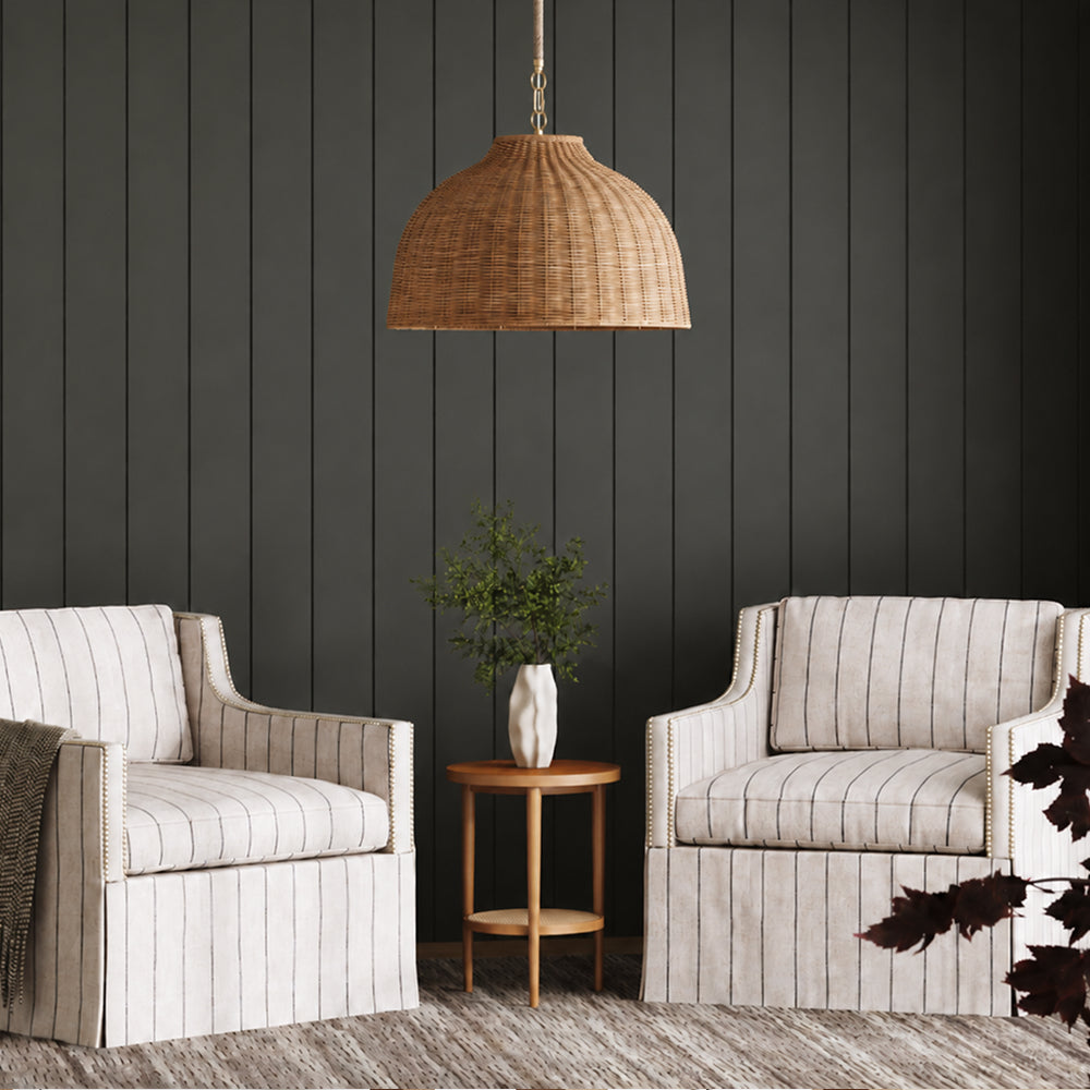 Two striped upholstered armchairs flanking a small wooden side table with a vase, beneath a large woven pendant light.