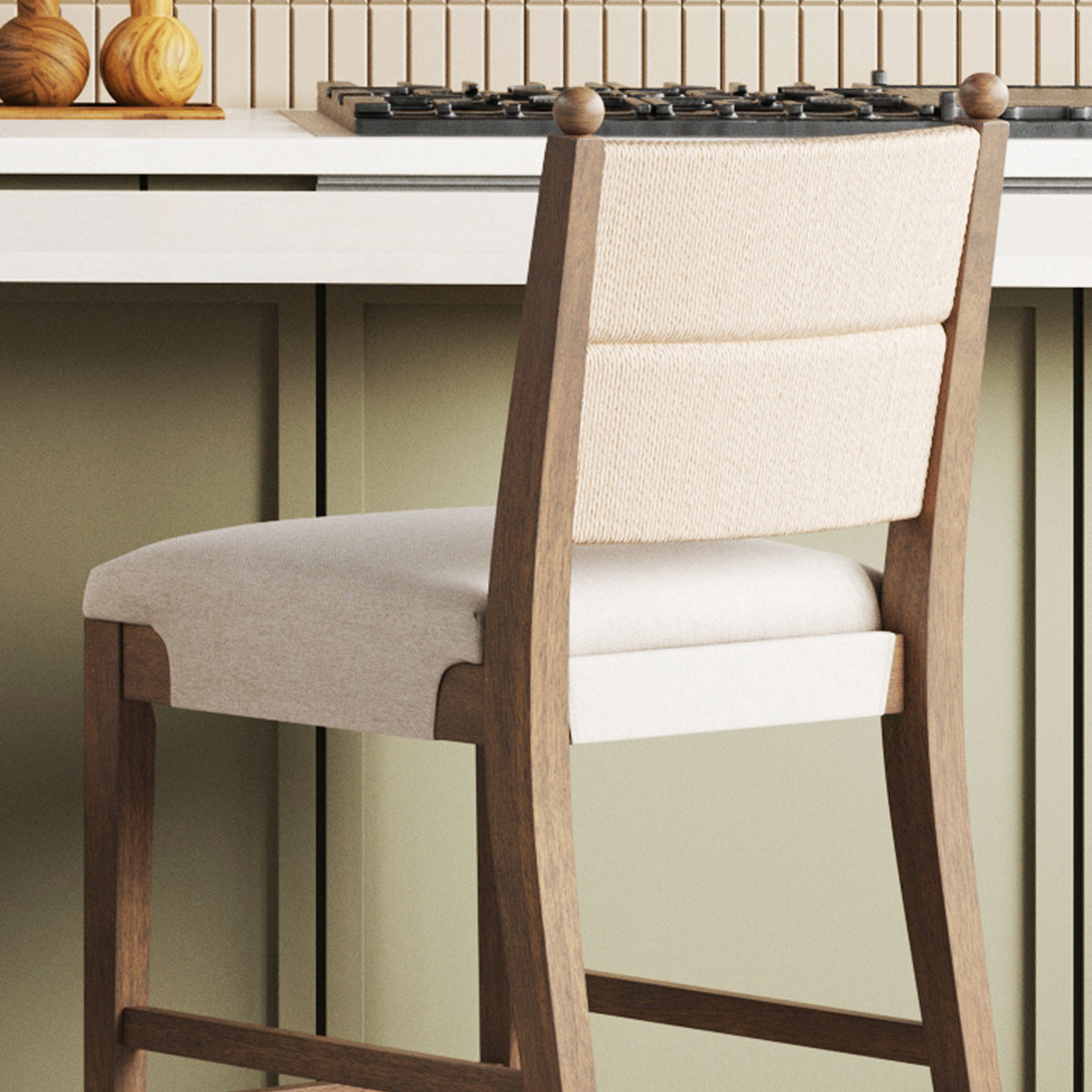 A wooden bar stool with an upholstered seat and backrest, positioned in front of a kitchen counter.