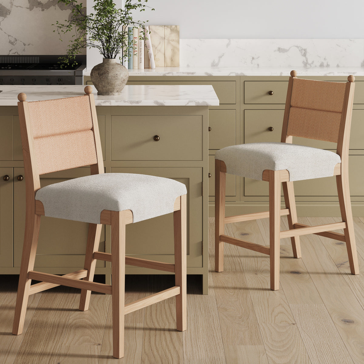 Two wooden counter stools with woven backrests and light grey upholstered seats positioned in front of a kitchen island.
