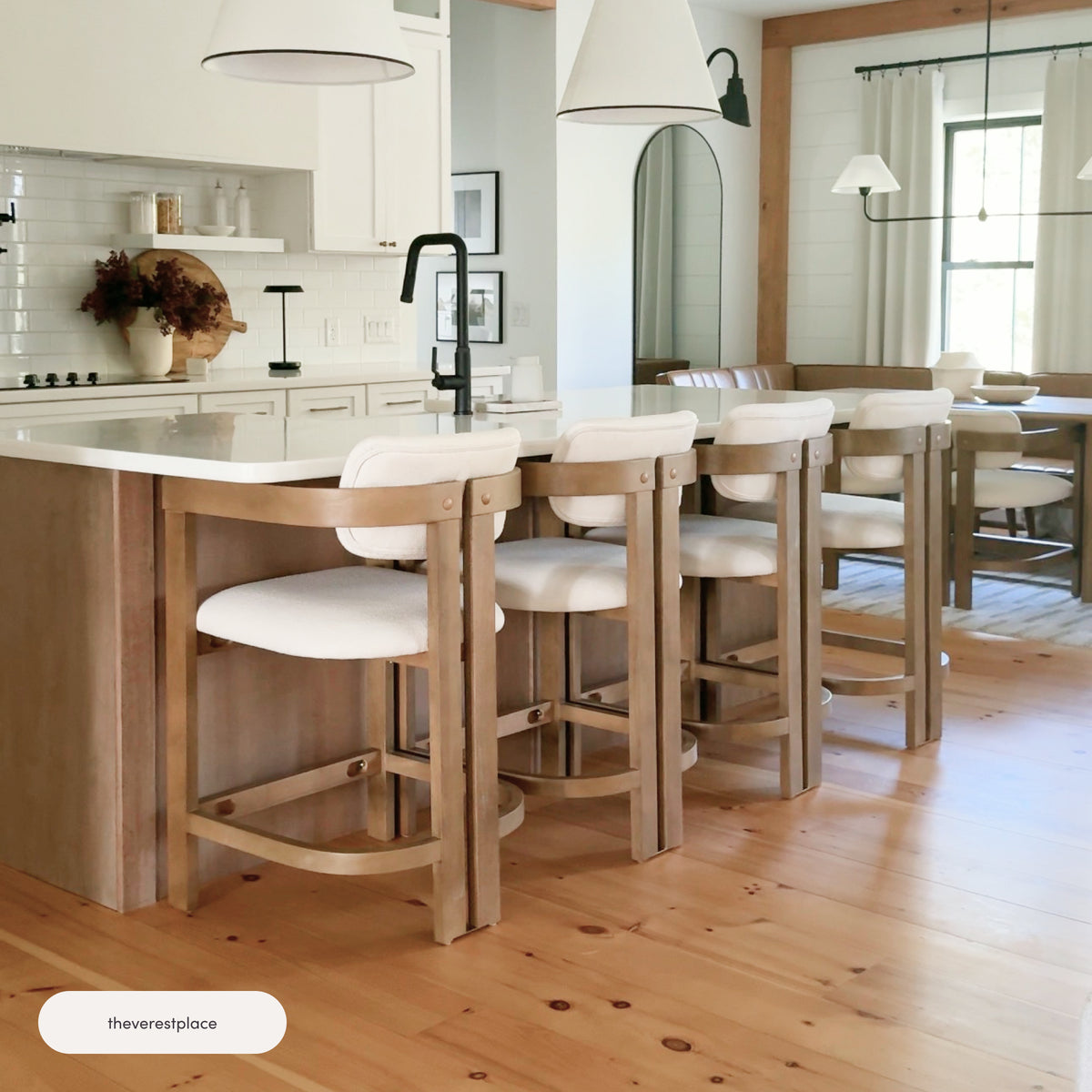 Four Nathan James Boucle Bar Stools with Barrel Back and Arm Light Brown in solid wood with curved barrel backs and white cushioned seats lined up at a kitchen island.