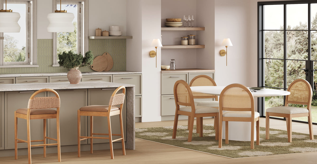 A modern kitchen featuring a central island with two stools, adjacent to a dining area with a round table and three chairs, all featuring cane back detailing.