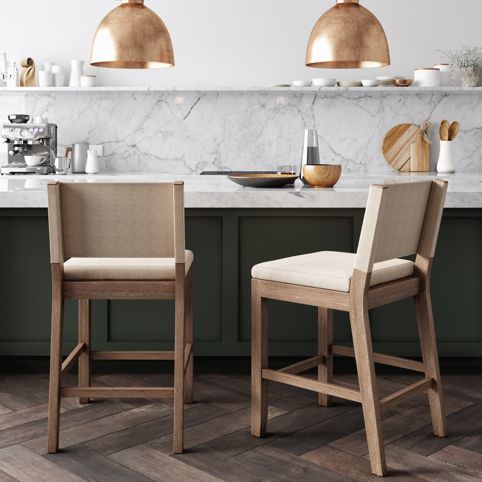 Two upholstered wooden bar stools sit at a marble kitchen counter with green cabinets, modern decor, and two copper pendant lights hanging above. A coffee machine and kitchenware are visible in the background.