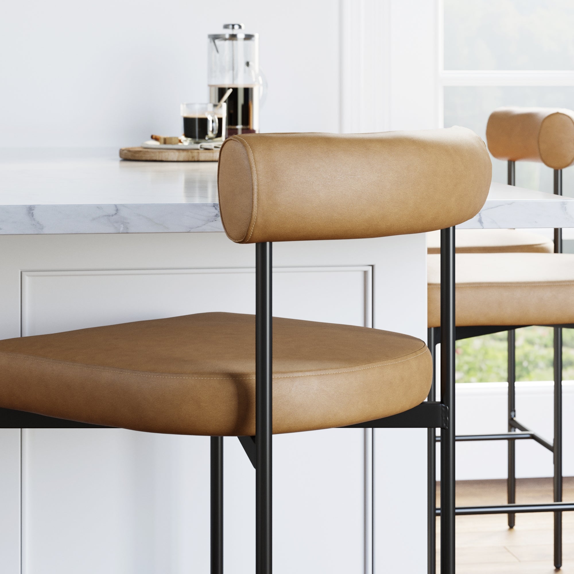 A tan leather barstool with a metal frame sits beside a white marble kitchen island. A French press, coffee cup, and tray are on the counter in the background near a bright window.