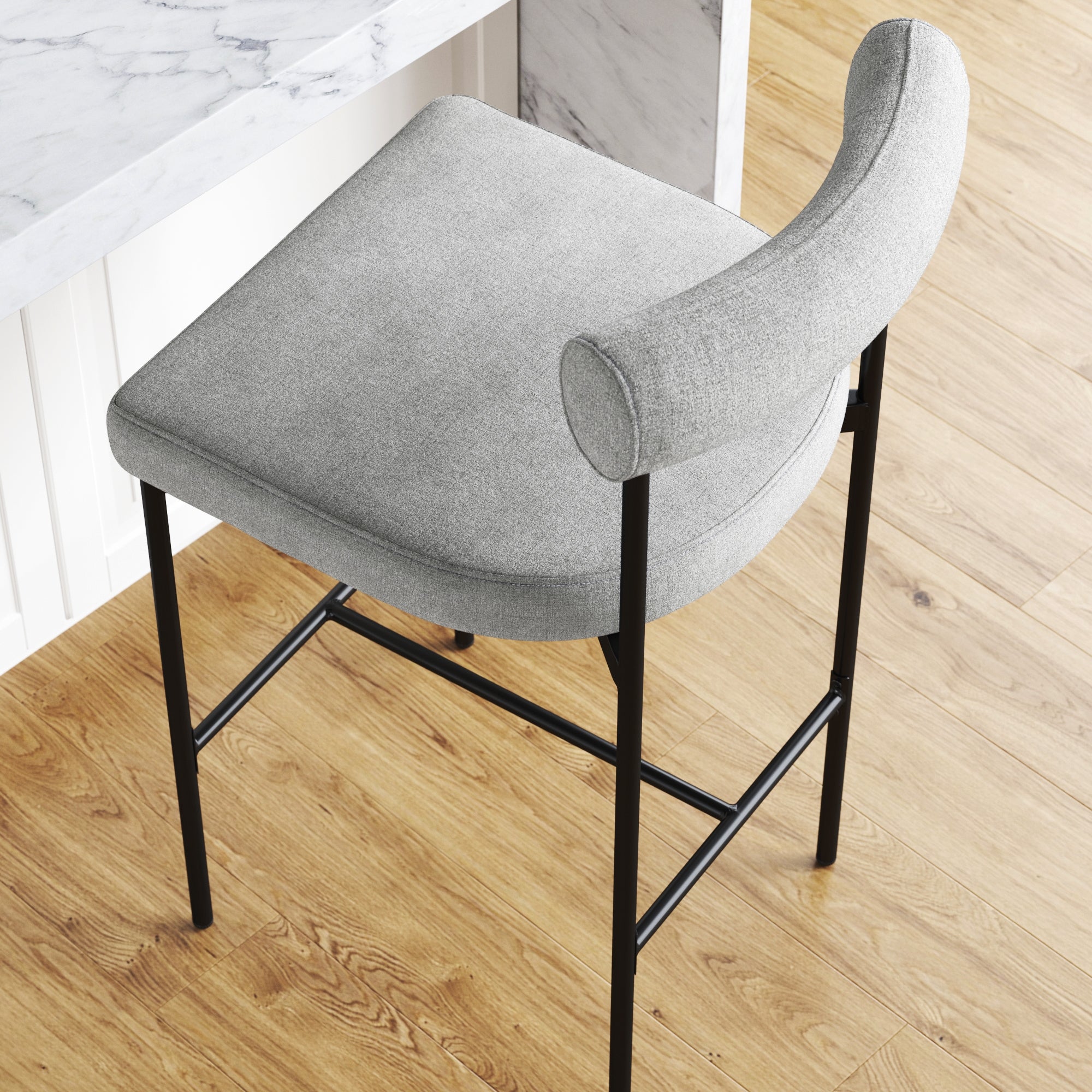 A modern bar stool with a light gray cushioned seat and curved backrest, featuring black metal legs, placed next to a white marble countertop on a light wood floor.