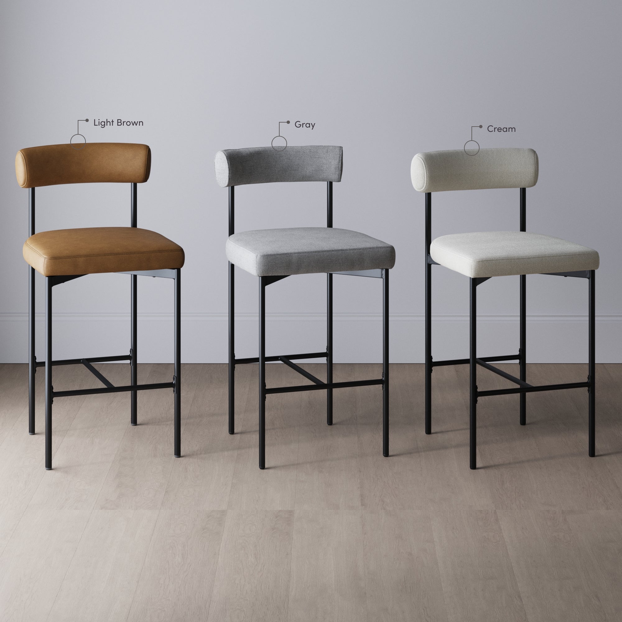 Three bar stools with metal legs are shown side by side against a light-colored wall. The seats and backs are upholstered in different colors: light brown, gray, and cream (left to right).