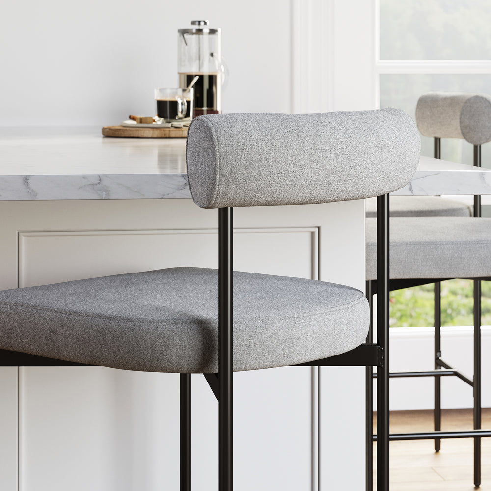 Two grey upholstered counter stools with black metal frames tucked under a marble kitchen island.