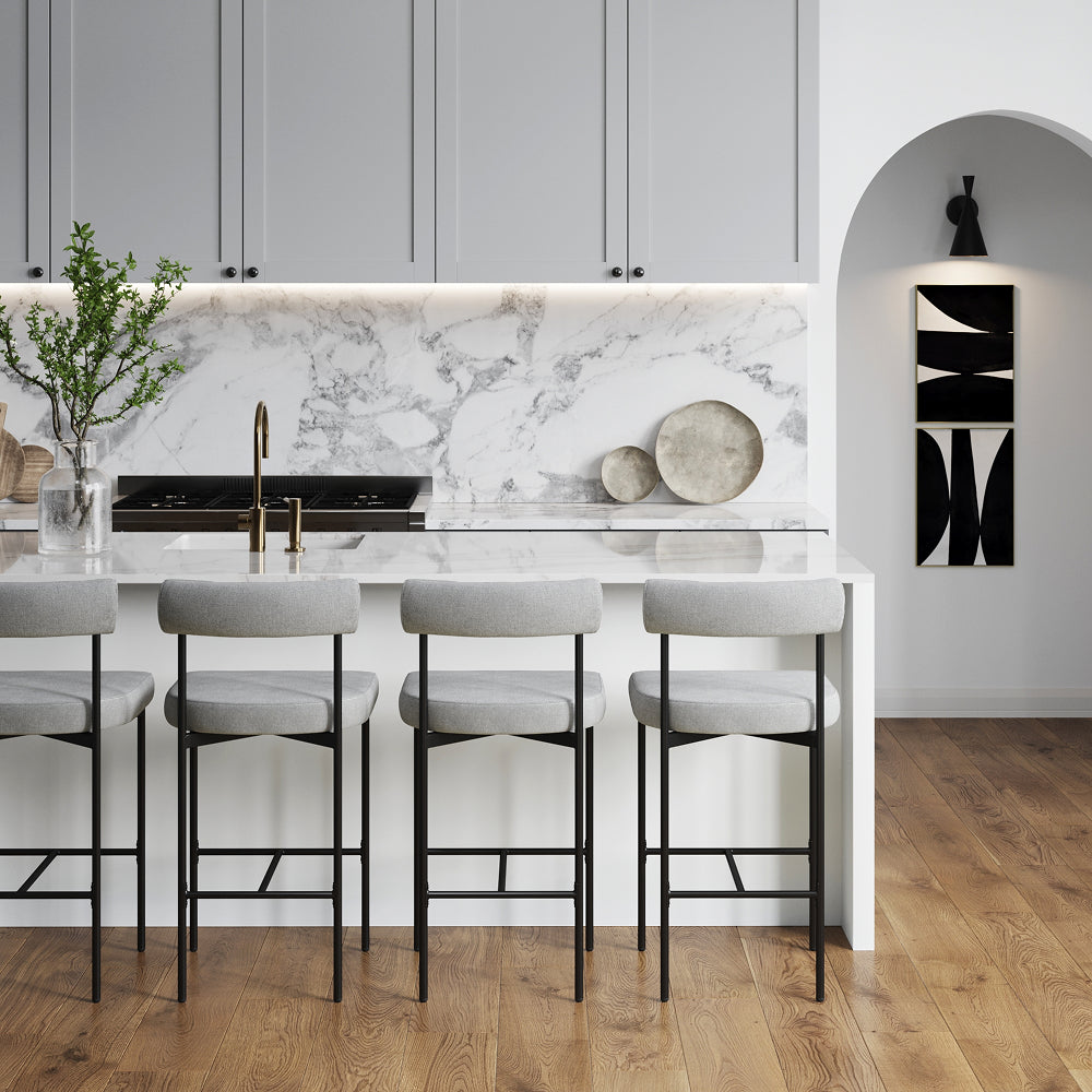A kitchen island with four gray stools sits in front of a white marble countertop, gray cabinets, and a doorway leading to a wall featuring abstract black and white art.