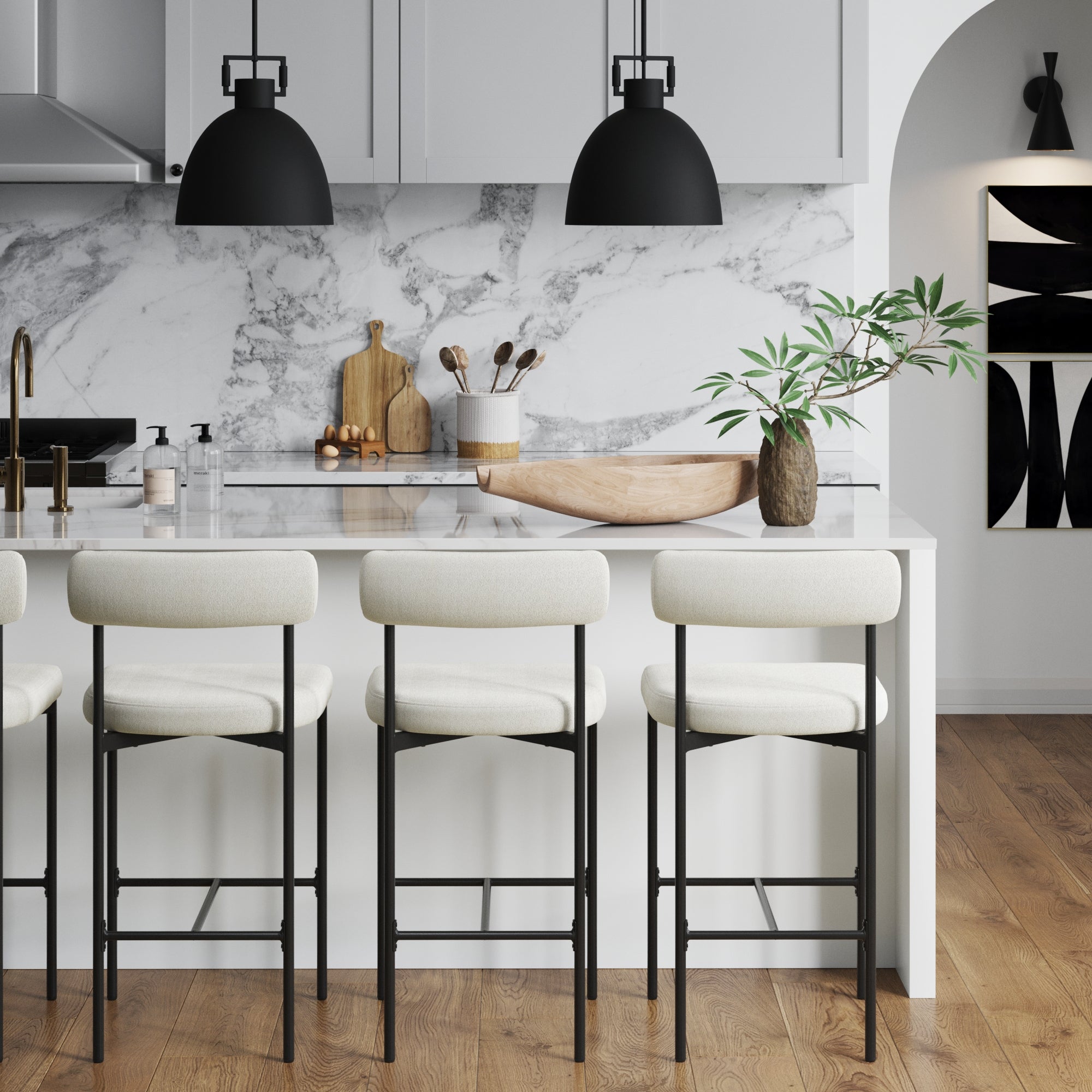 A modern kitchen with white cabinetry, marble backsplash, a white island with four cushioned barstools, black pendant lights, wood accents, and a vase with greenery on the counter.