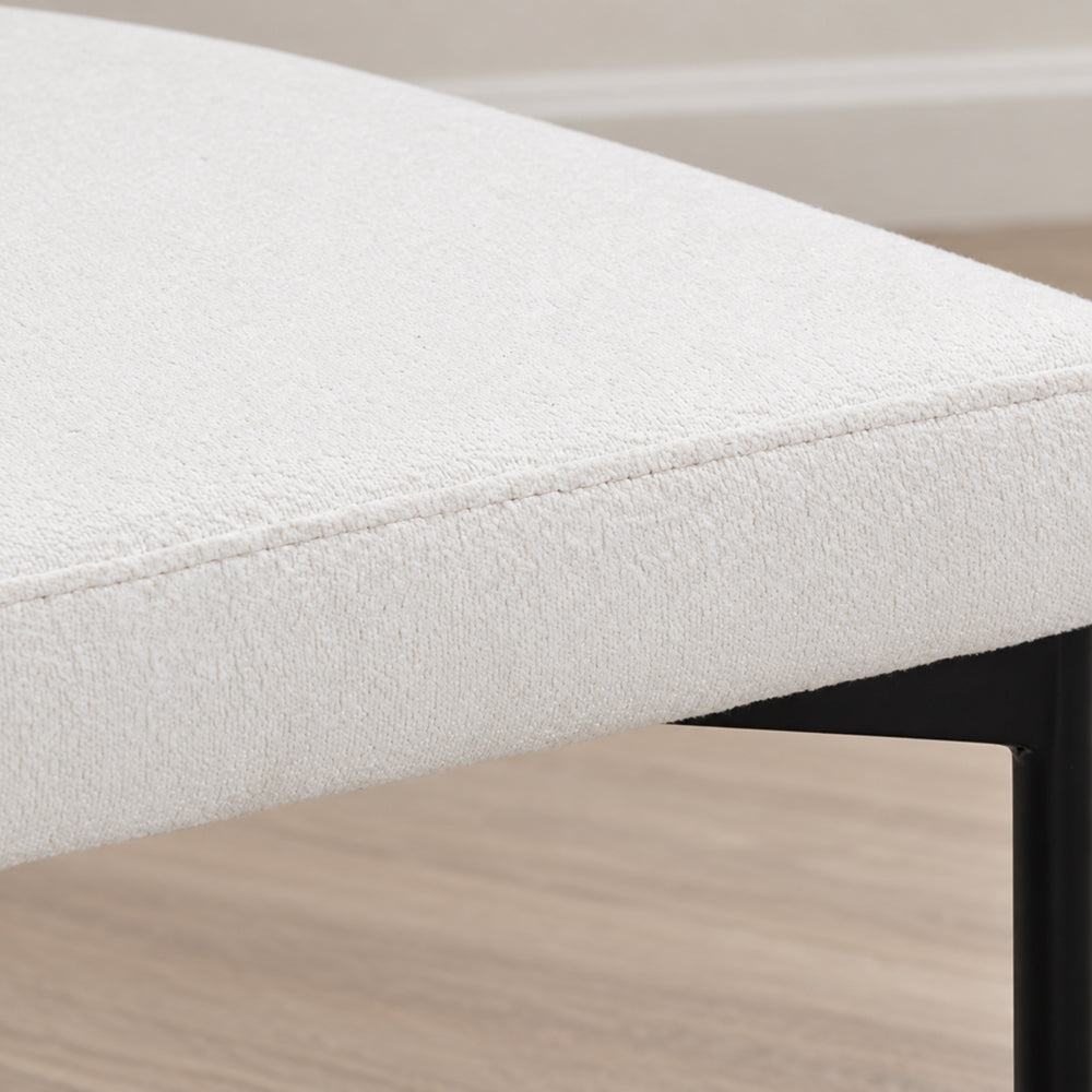 Close-up of a white upholstered bench seat with black metal legs.