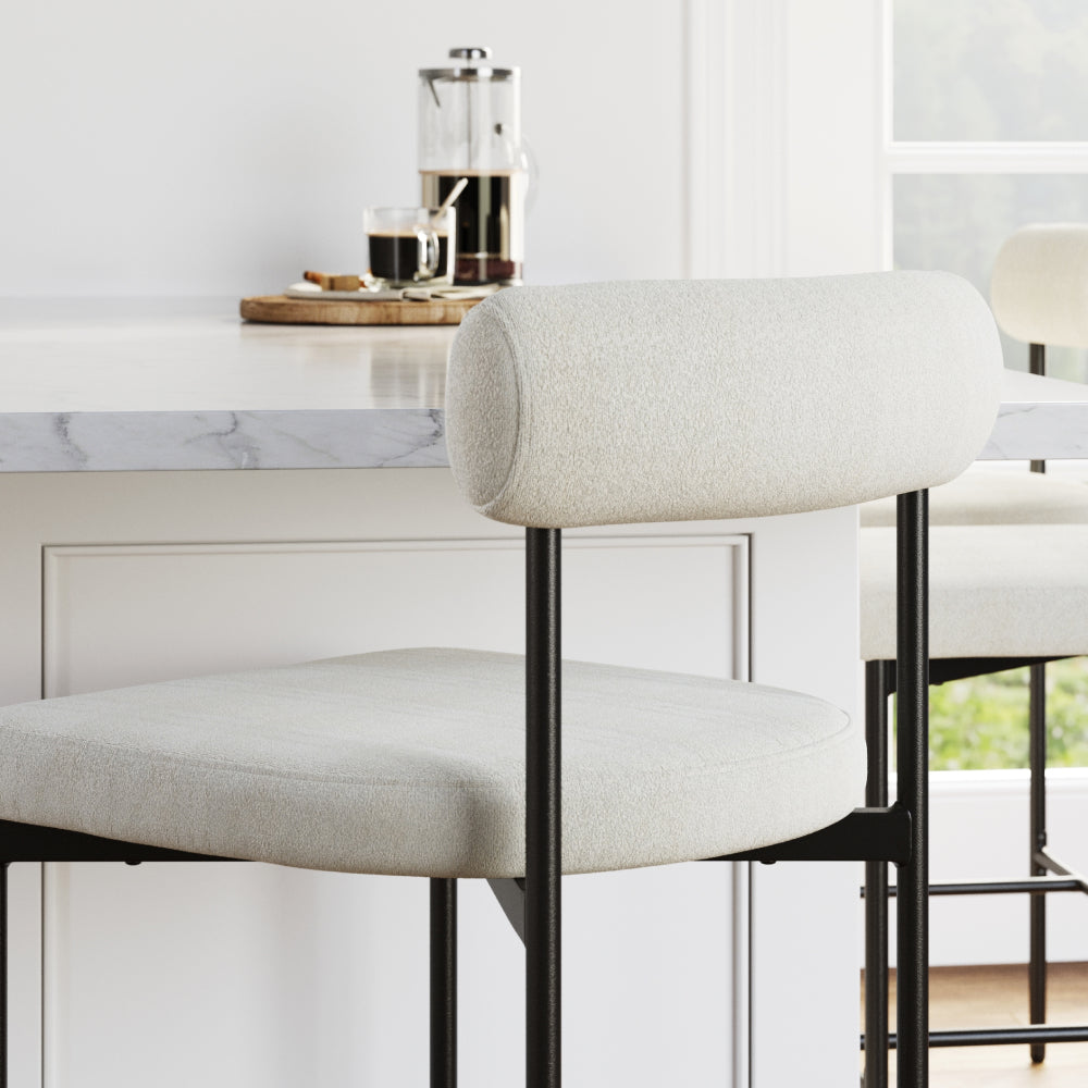 Two off-white upholstered bar stools with black metal frames tucked under a kitchen island.