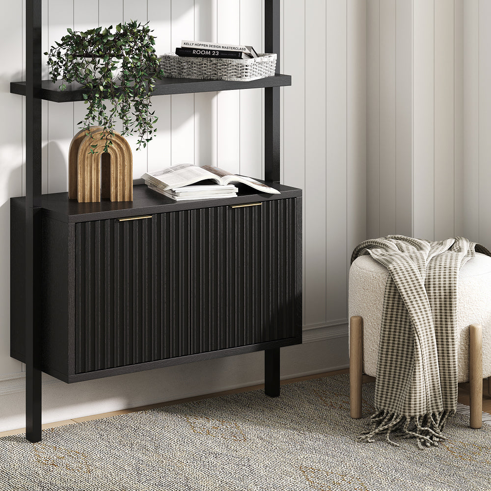 A black storage cabinet with vertical ribbed doors mounted on a black metal frame, with a small stool and checkered throw blanket placed next to it.