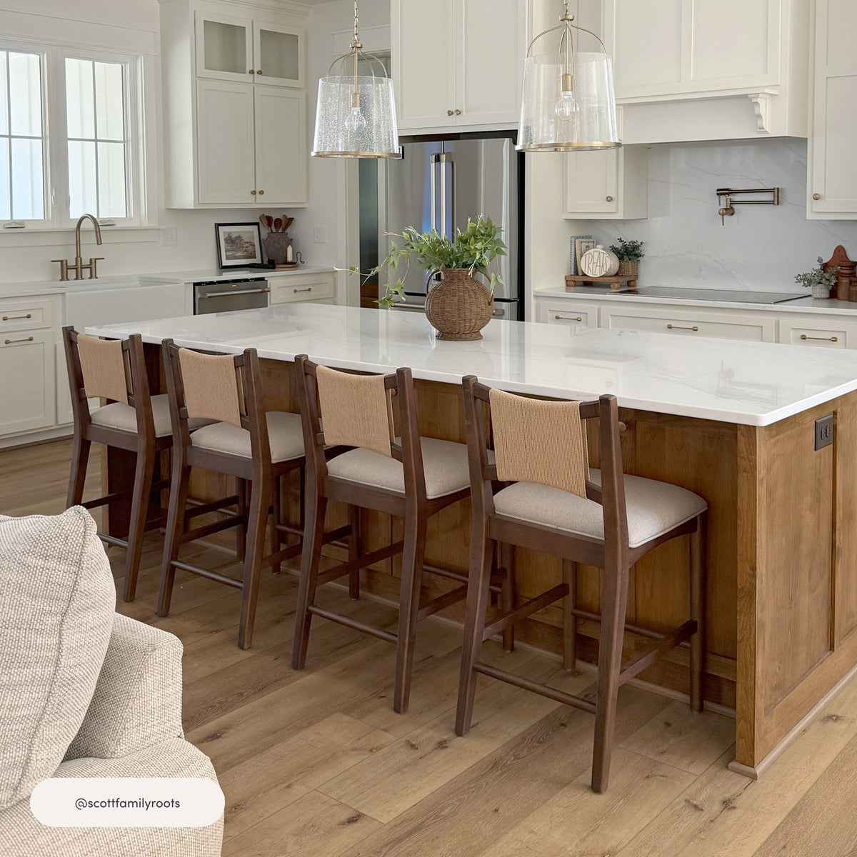 Four Nathan James Modern Seagrass Back Arched Wood Counter Stool Medium Brown counter stools with solid wood frames and synthetic seagrass backrests arranged along a kitchen island.