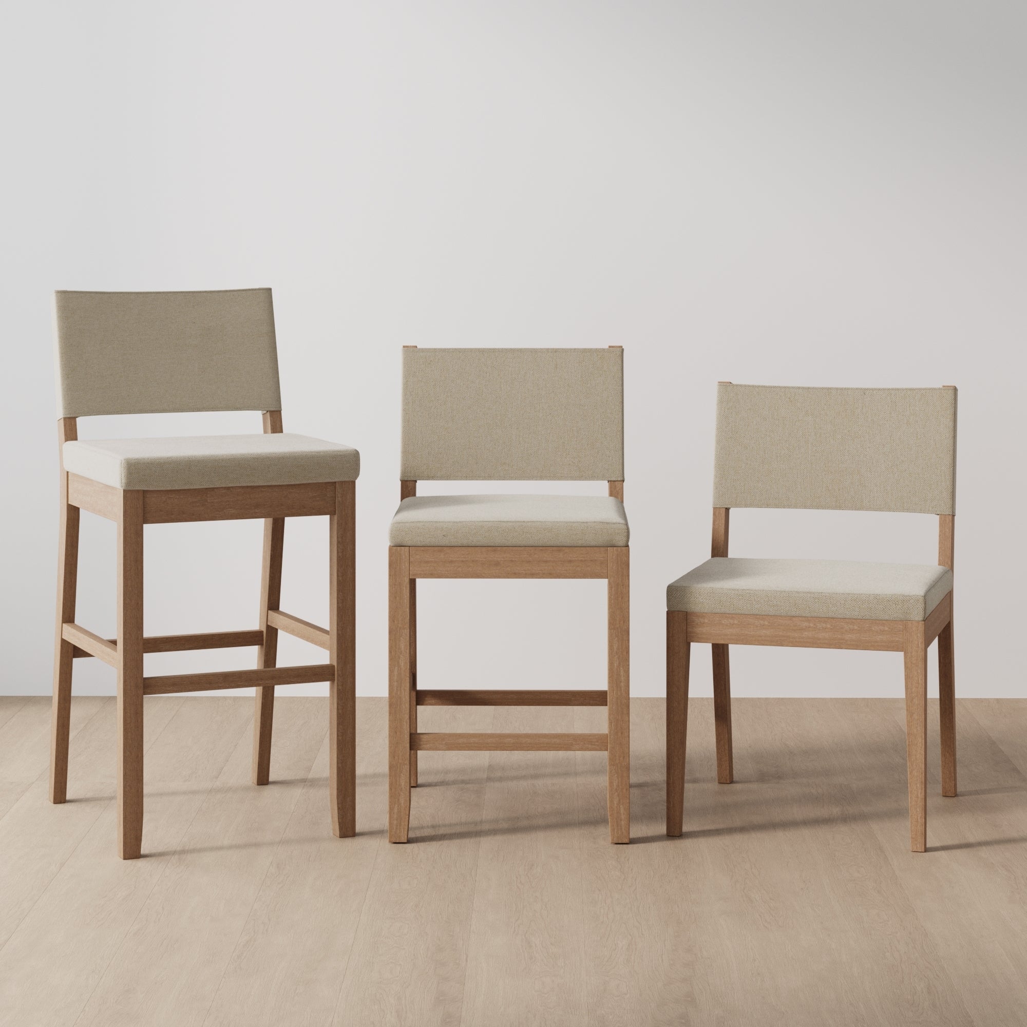 Three wooden chairs with beige upholstered seats and backs are arranged side by side. The chairs vary in height: one is a bar stool, one is a counter stool, and one is a standard dining chair. The background is plain.