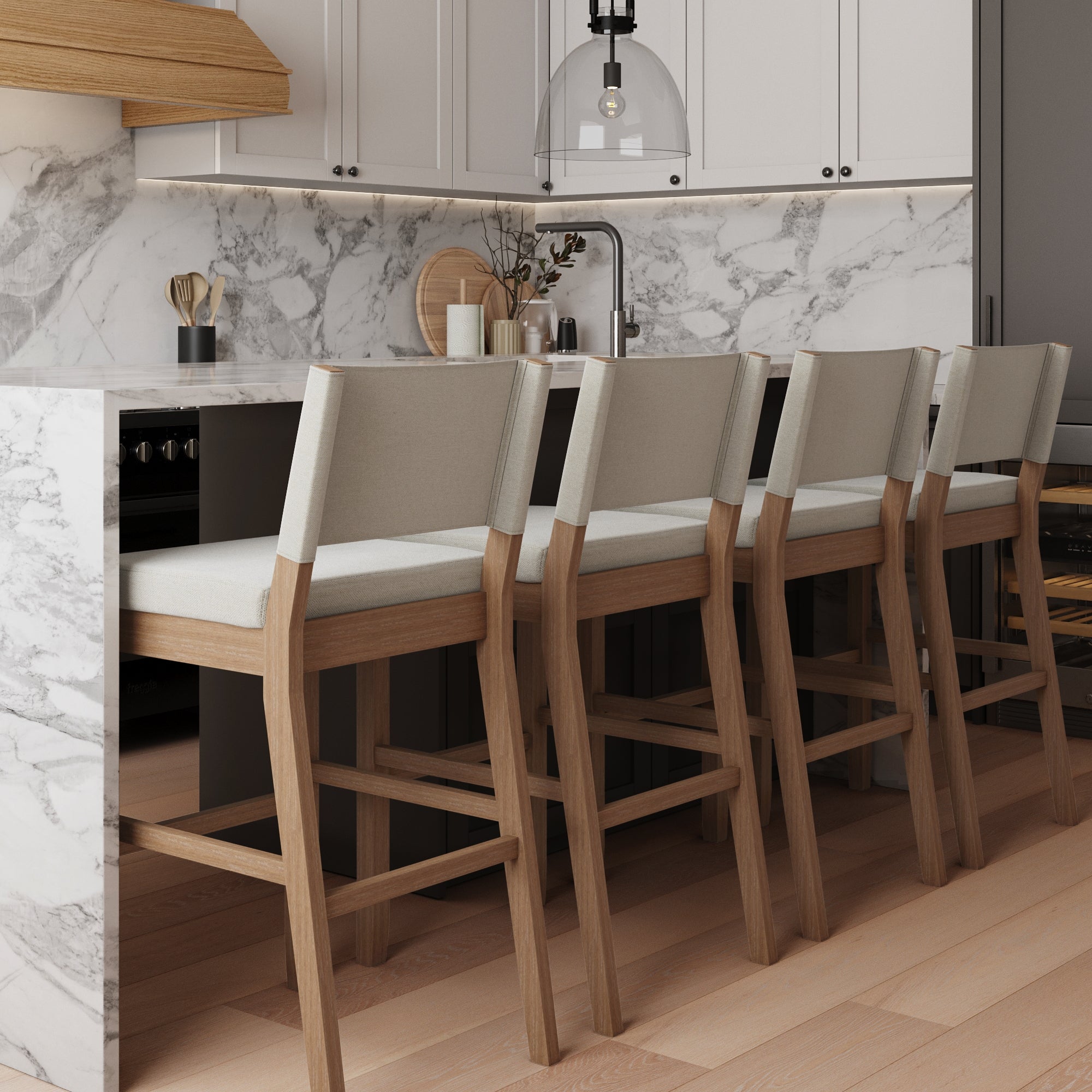A modern kitchen with a marble island, four wooden bar stools with light cushions, white cabinets, a marble backsplash, and a glass pendant light above the counter.