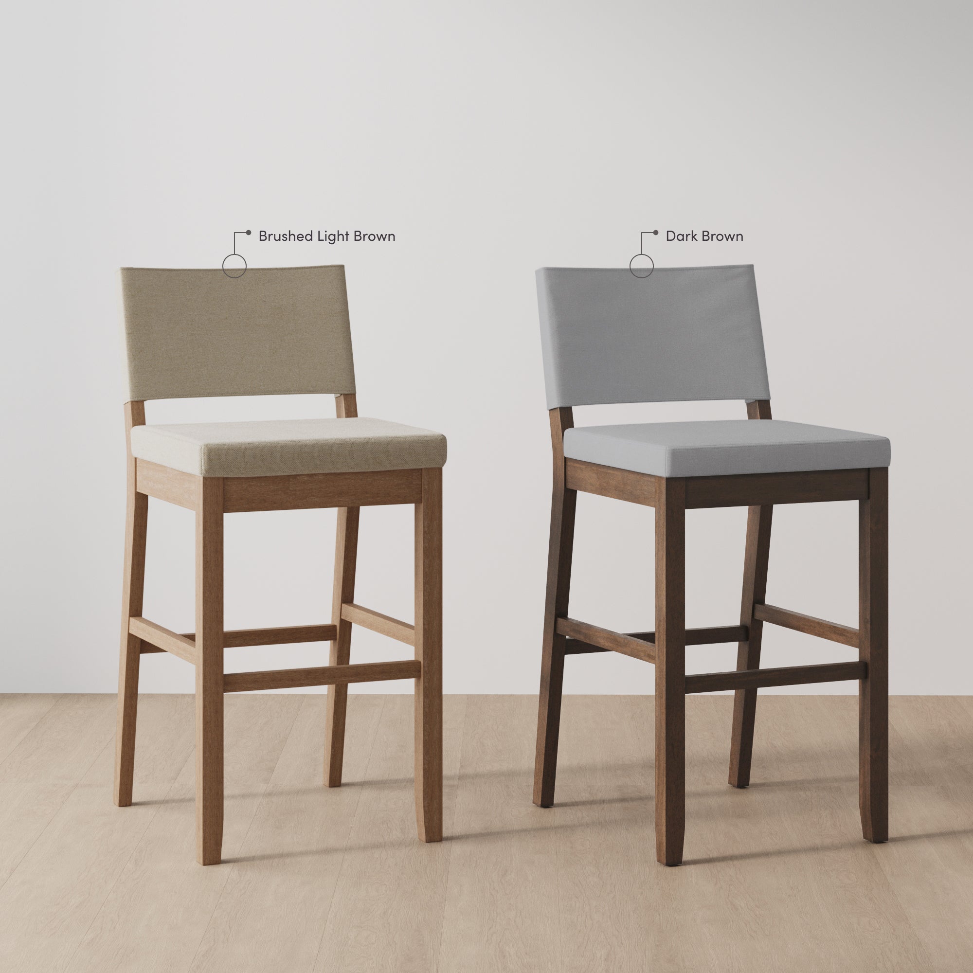Two wooden bar stools are side by side; the left has a brushed light brown fabric seat and back, and the right has a dark brown fabric seat and back. The stools have different wood finishes.