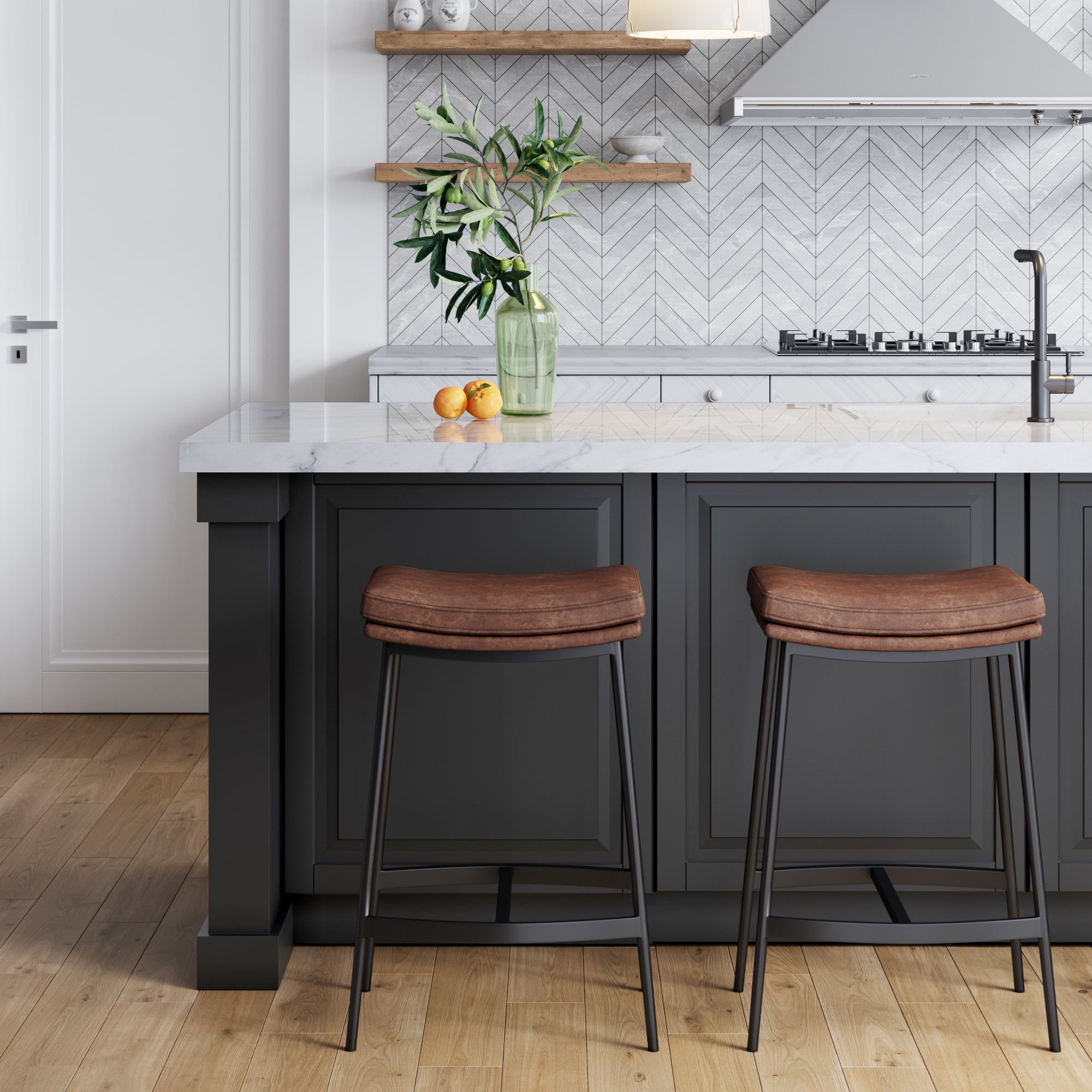 Modern kitchen with a gray island, two brown cushioned bar stools, a vase with green branches, oranges on the counter, wood flooring, and a white chevron tile backsplash with open shelves and a range hood.