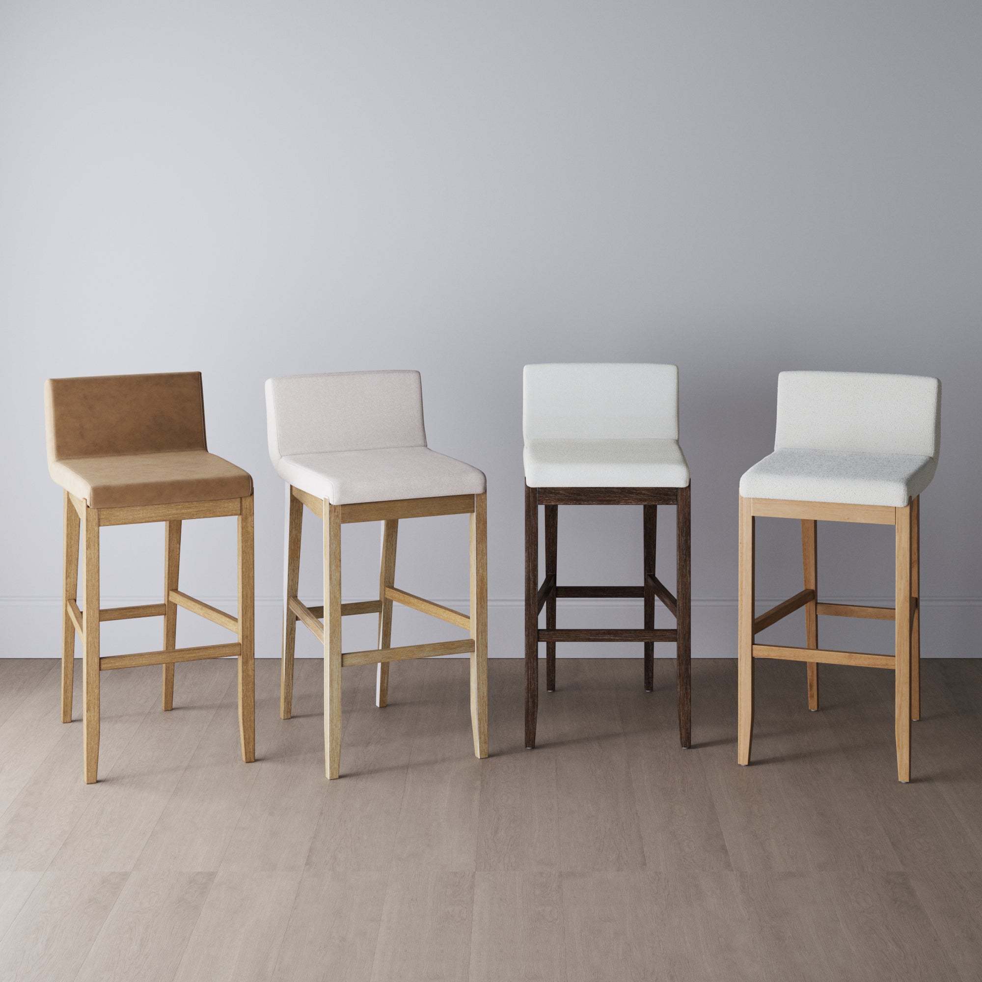 Four wooden bar stools with upholstered seats and low backs are arranged side by side against a light gray wall, each featuring a different color of wood and fabric. The floor is a light wood tone.