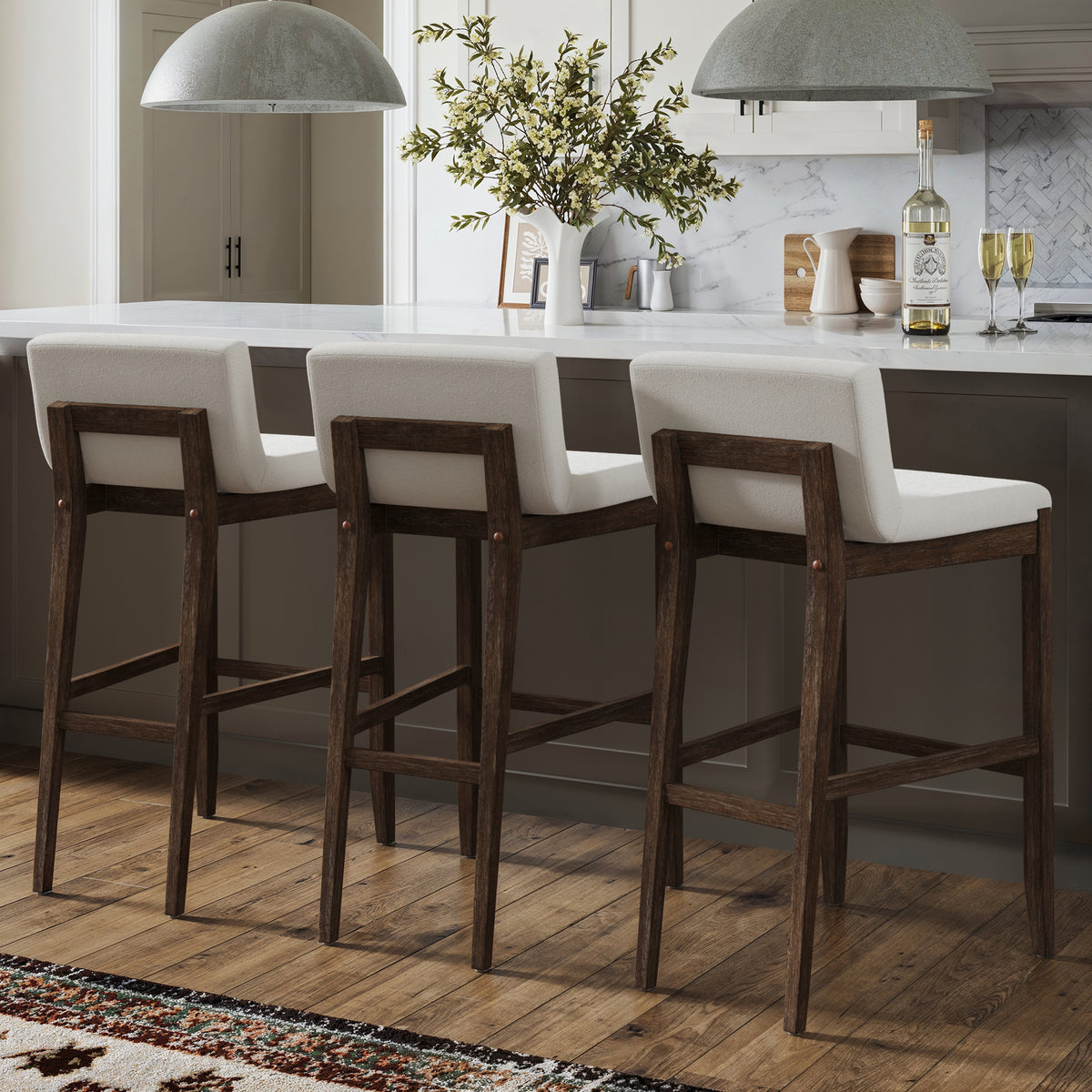 Three wooden bar stools with upholstered white seats arranged at a kitchen island.