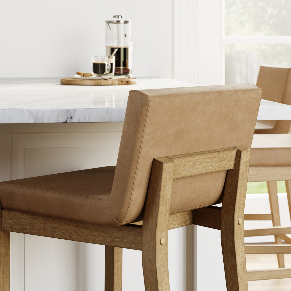 Tan upholstered bar stools with wooden frames tucked under a marble-topped kitchen island.