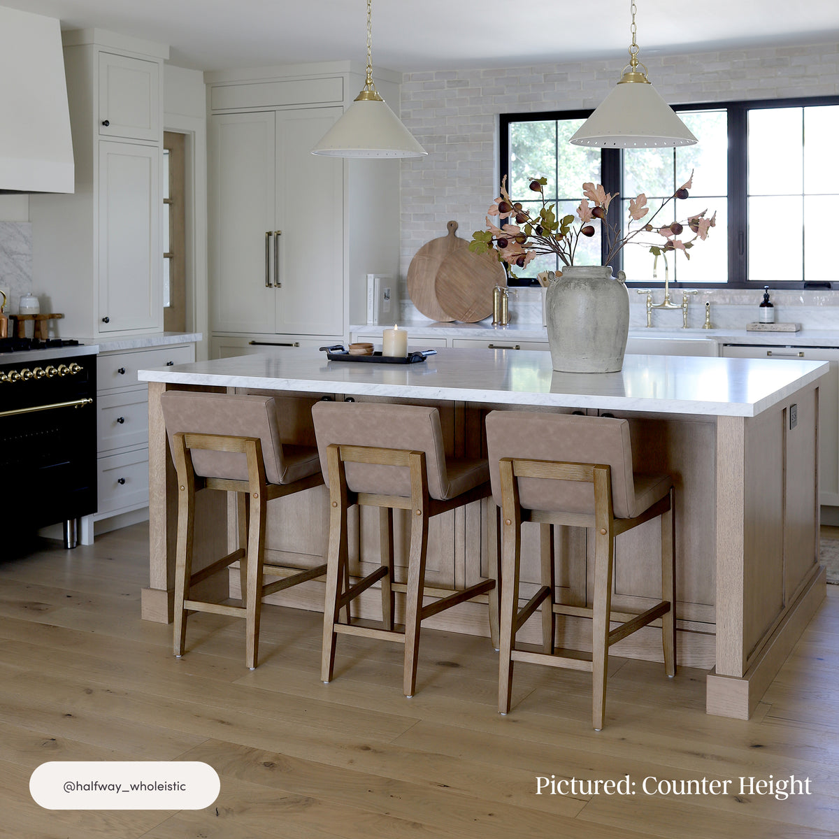 Three Nathan James Exposed Wood Back Bar Stools Light Brown tucked under a marble-topped kitchen island, featuring light wood frames and padded C-shape cushions.