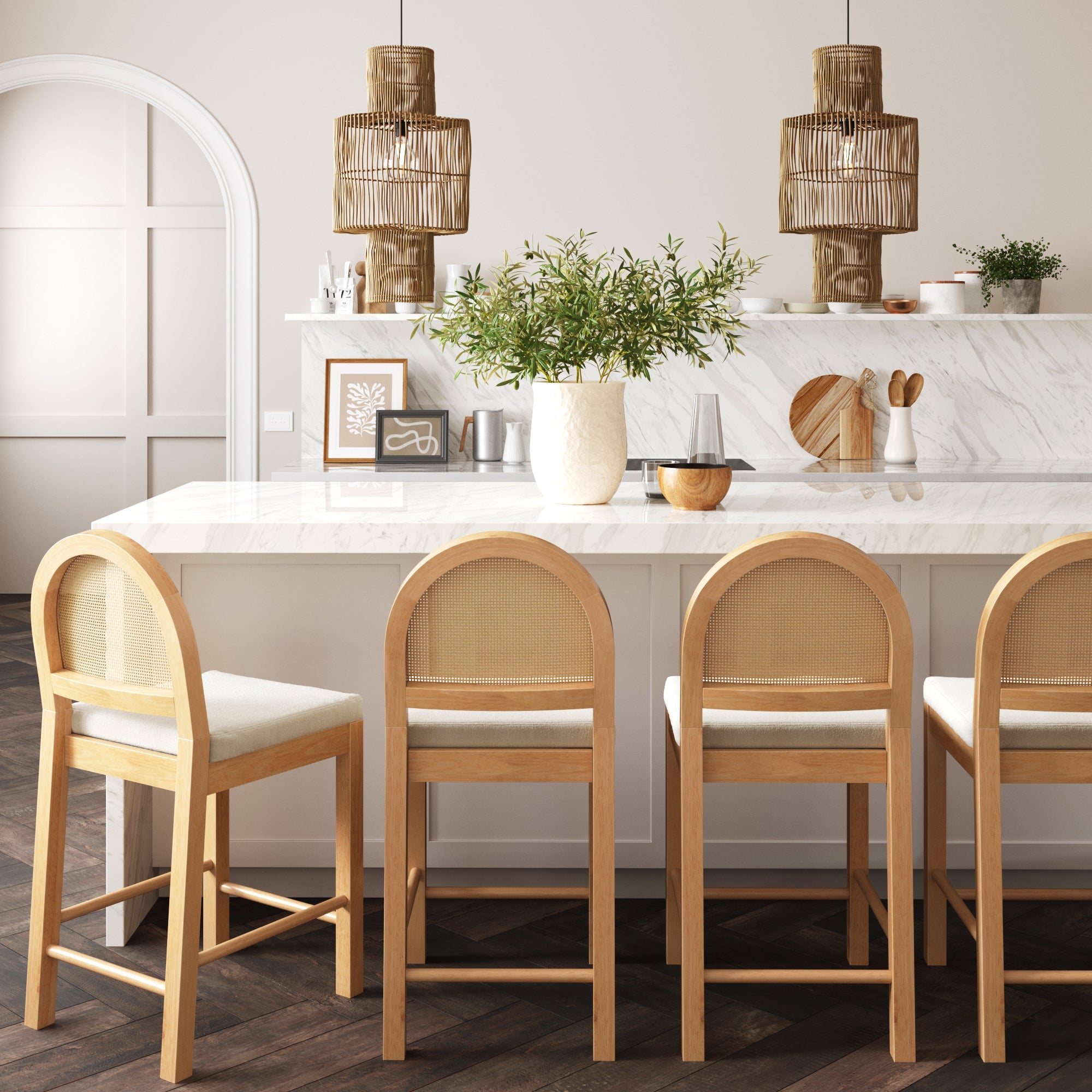 A modern kitchen with a marble island, four wooden bar stools with light cushions, potted plant centerpiece, and woven pendant lights hanging above. Neutral tones and clean, minimal decor create a warm, inviting space.